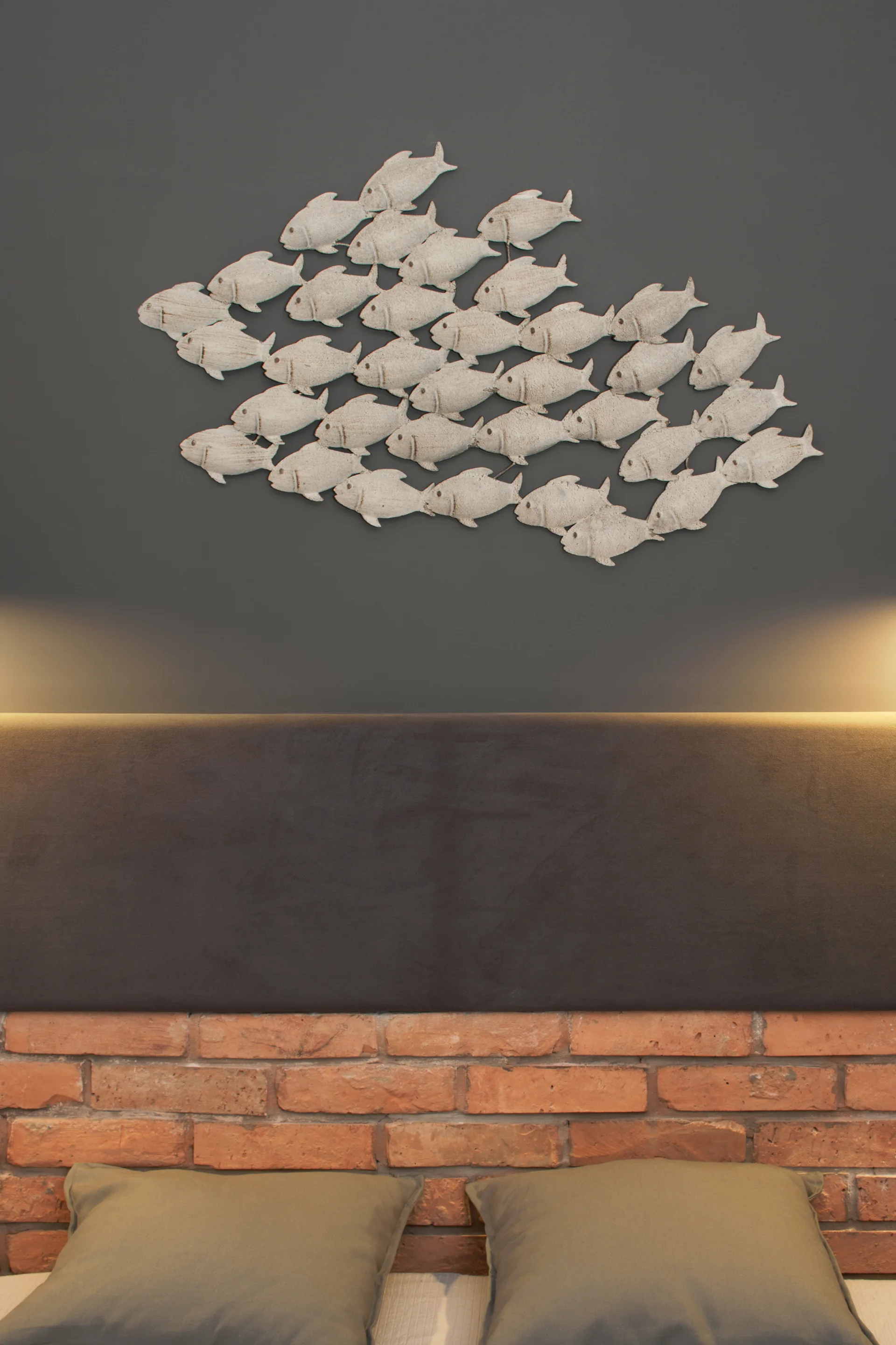 A dark gray upholstered headboard is mounted above an exposed brick wall, highlighted by glowing accent light and a fish sculpture.