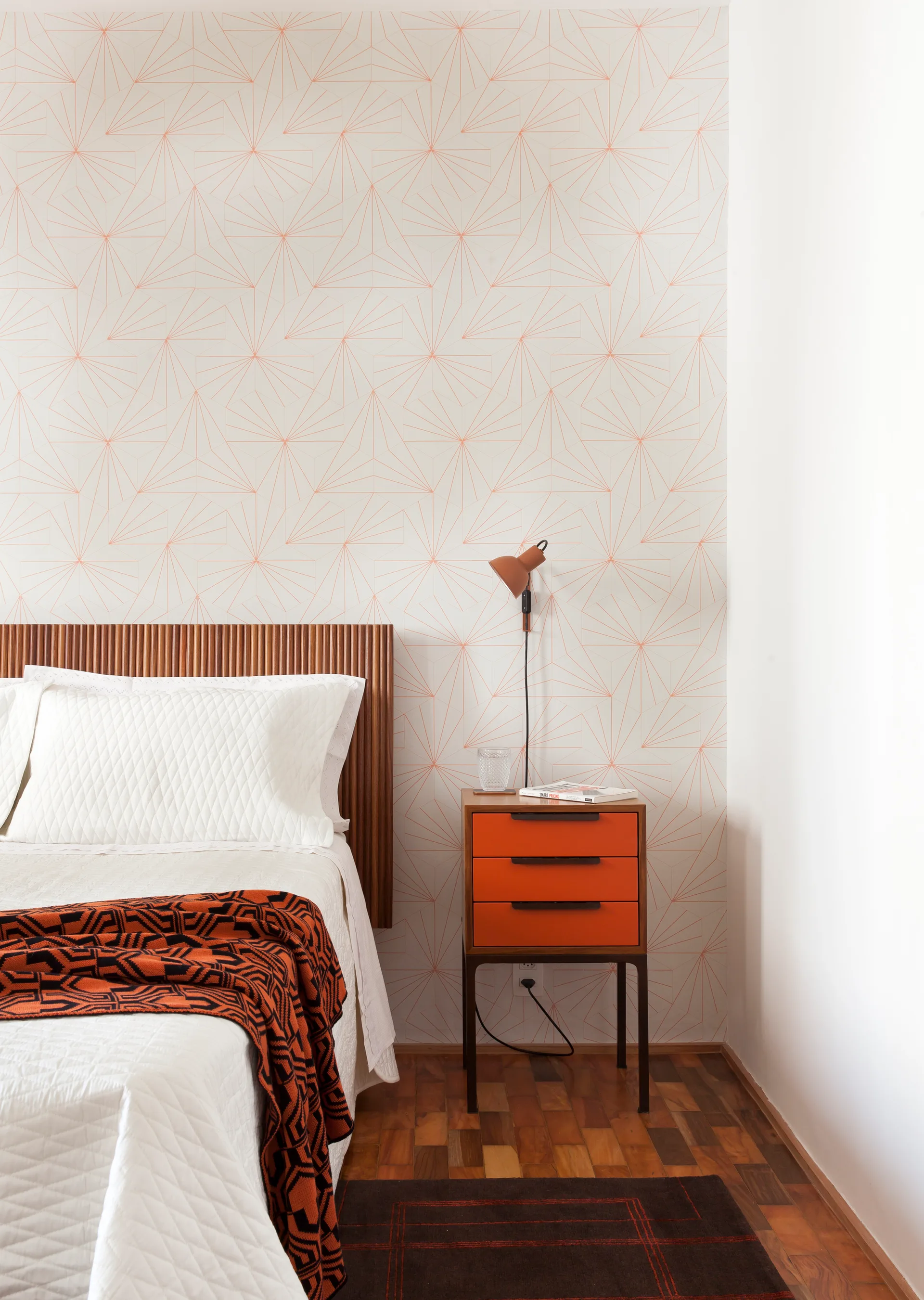 A bedroom corner features a fluted wood headboard, geometric line wallpaper, and a wood nightstand with bright orange drawers.