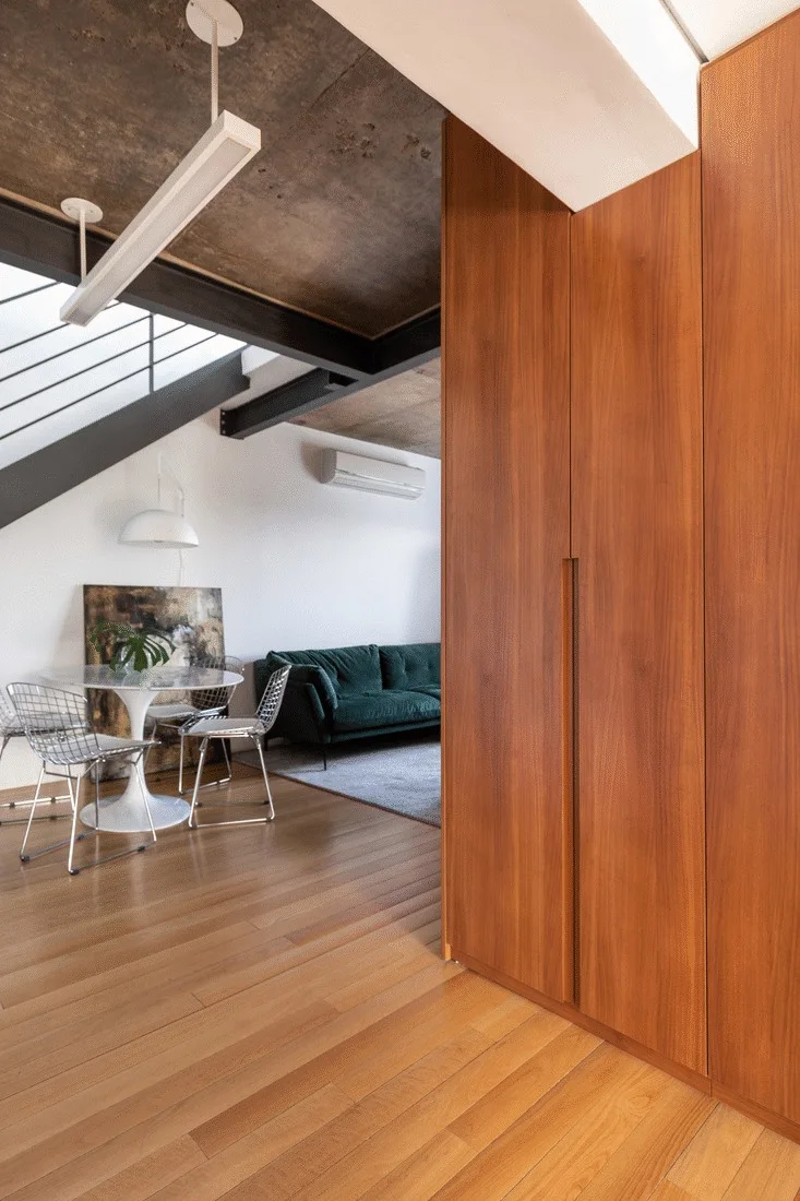 An open living space featuring warm wood flooring, built-in cabinets, a pedestal dining table, and a green sofa beneath a concrete ceiling.