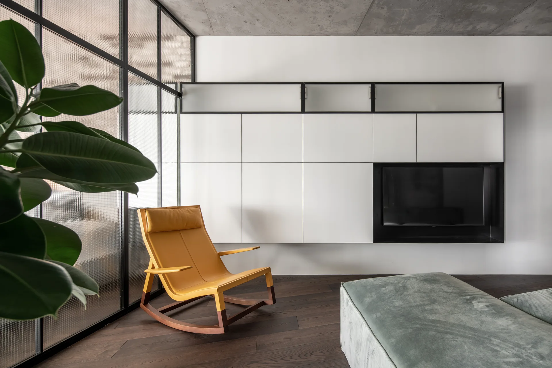 A minimalist living room featuring a bold yellow leather rocking chair beside a metal grid partition and a large wall of custom white cabinets.