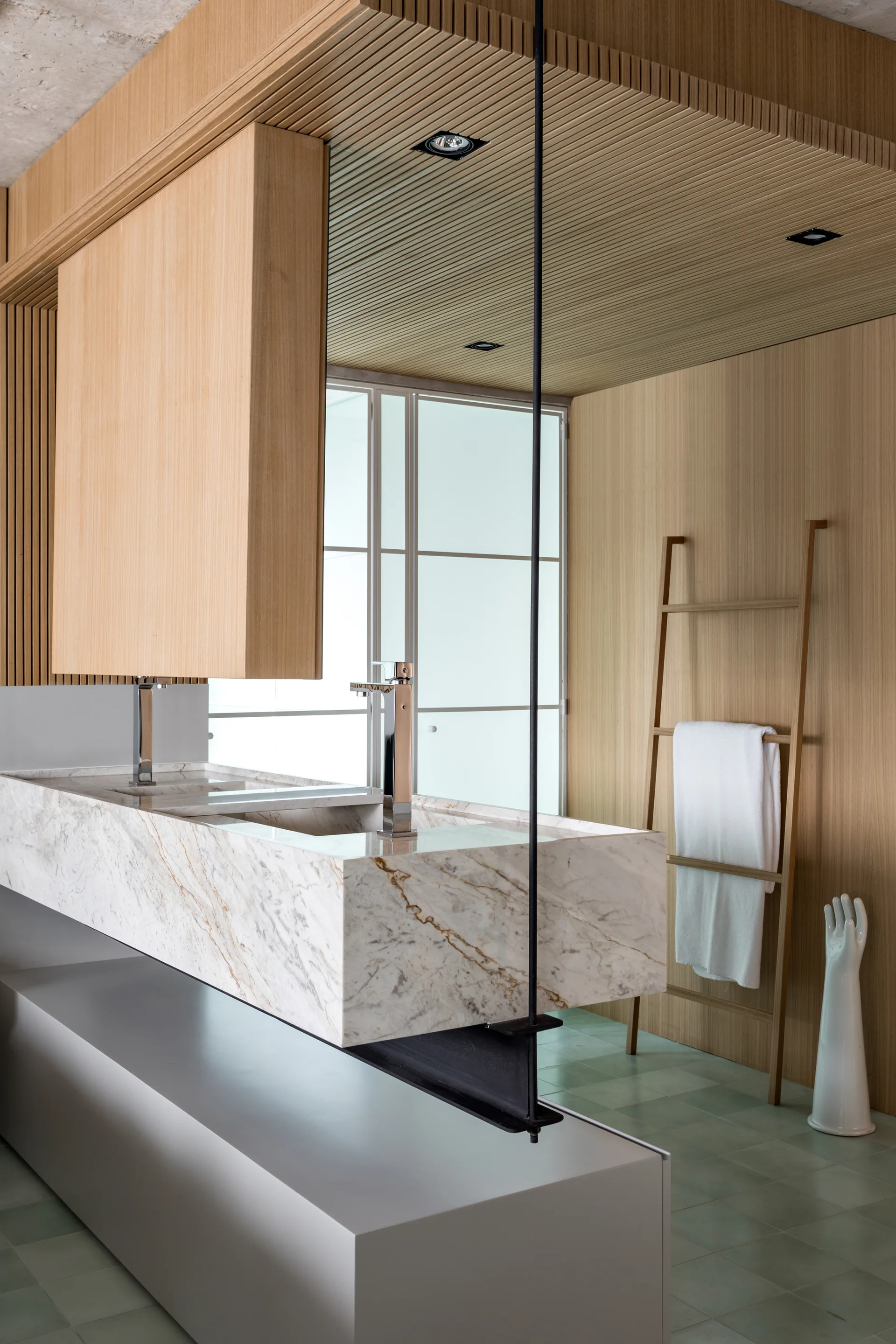 A modern bathroom features a floating marble vanity, vertical wood slat walls and ceiling, a wooden towel ladder, and light green tiled flooring.
