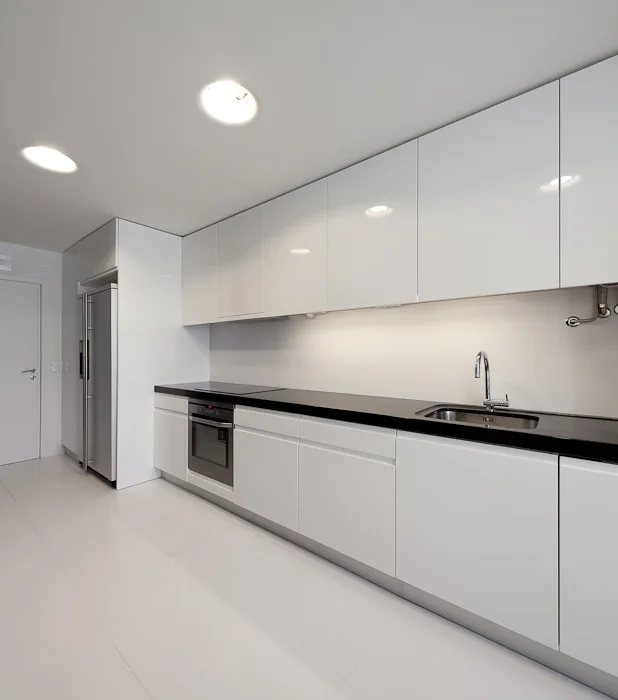 A minimalist kitchen featuring glossy white slab cabinets, a dark black countertop with an undermount sink, and integrated stainless steel appliances.