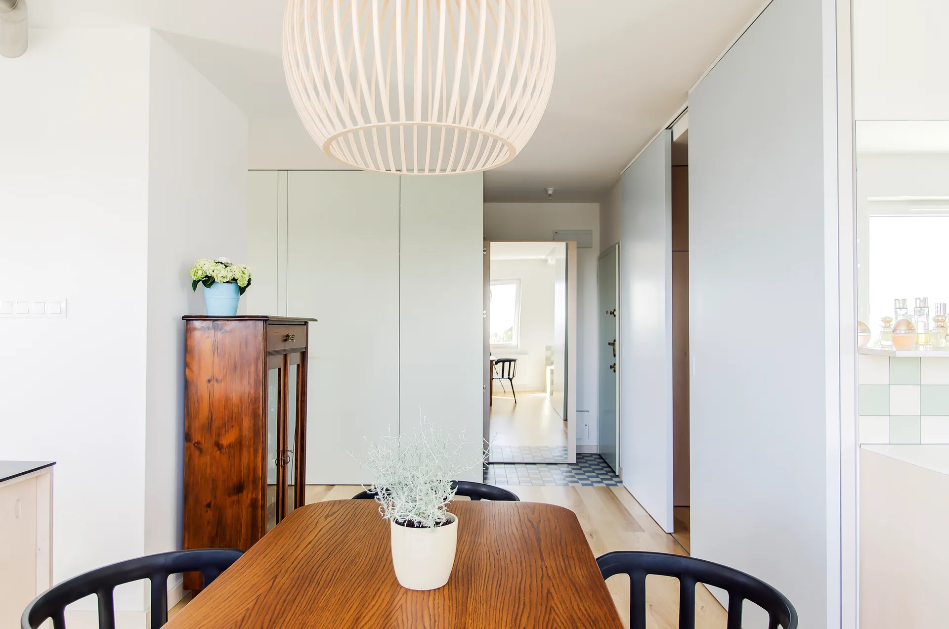 A bright dining room features a wooden table with black spindle chairs under a large white slatted spherical pendant light next to light sliding doors.
