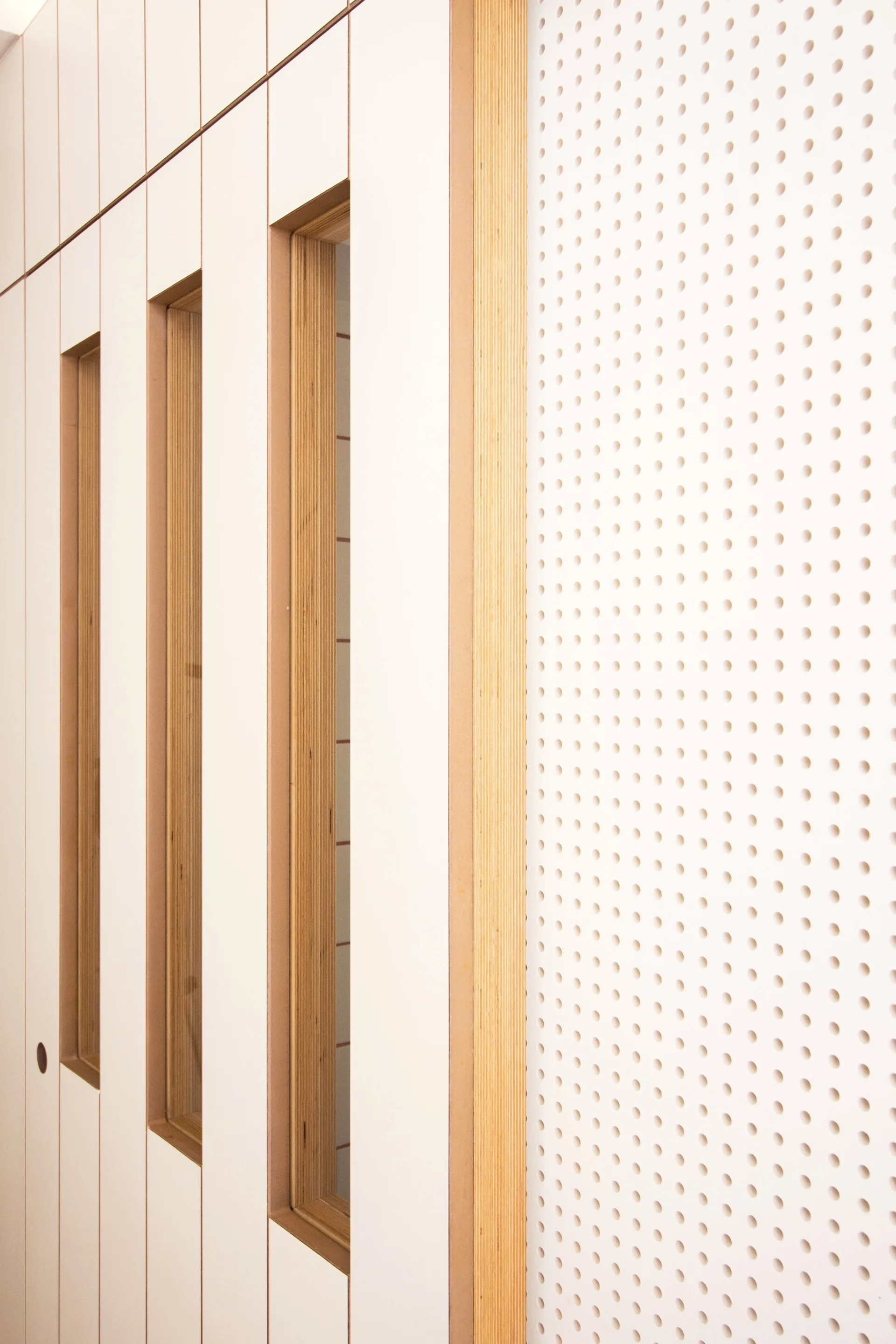Custom white cabinetry featuring exposed plywood edges and vertical cutout pulls sits adjacent to a white perforated pegboard wall panel.