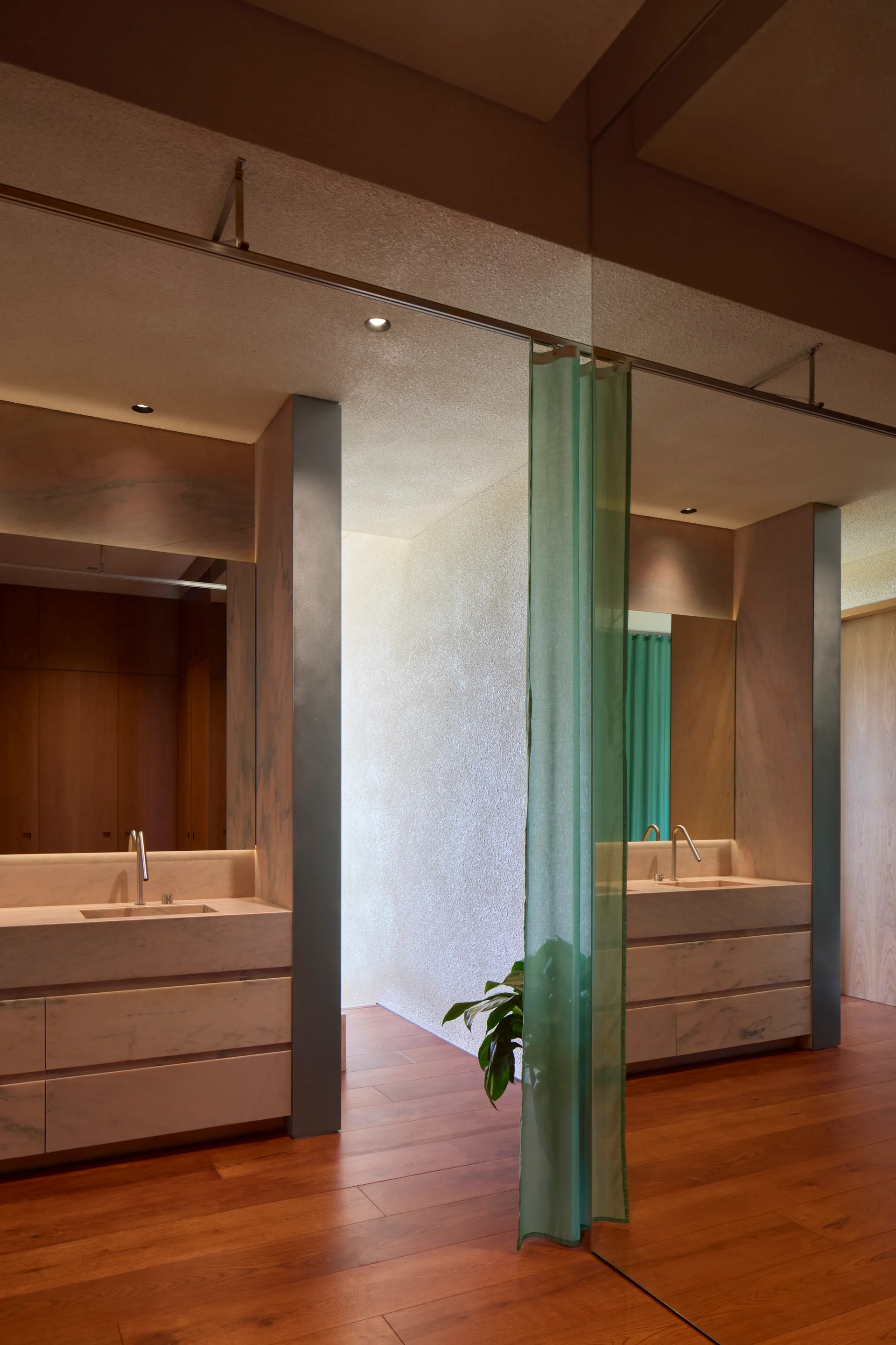 A modern bathroom features a white marble vanity with an integrated sink, warm wood flooring, a textured wall, and a translucent green curtain.