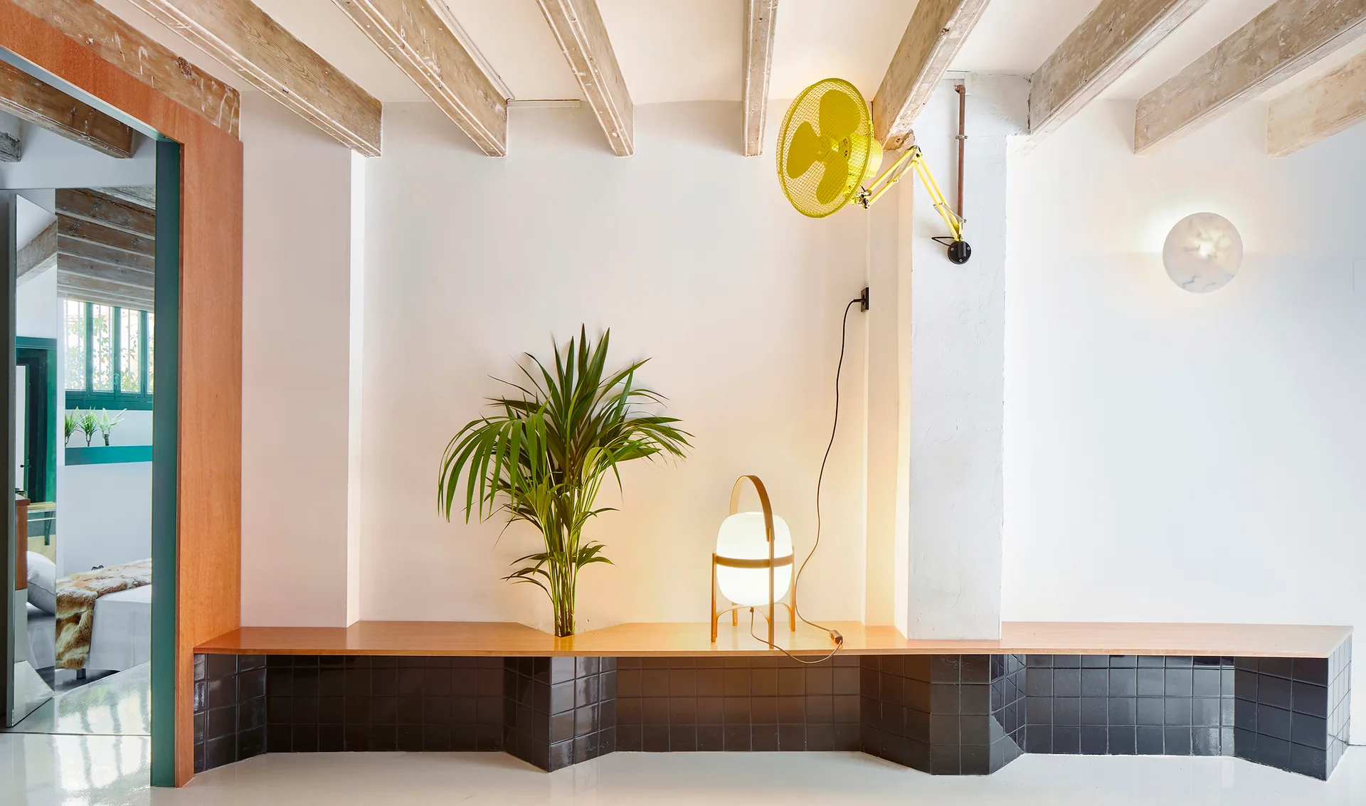 A long built-in bench with a black tiled base and wood top runs along a white wall beneath exposed wooden ceiling beams.
