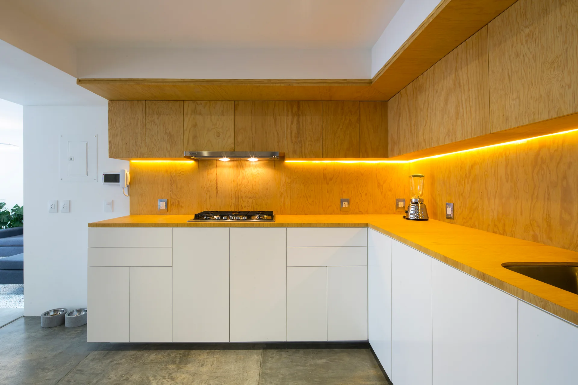 A modern kitchen featuring white lower cabinets, warm wood countertops, a matching wood veneer backsplash, and a glowing yellow LED light strip.