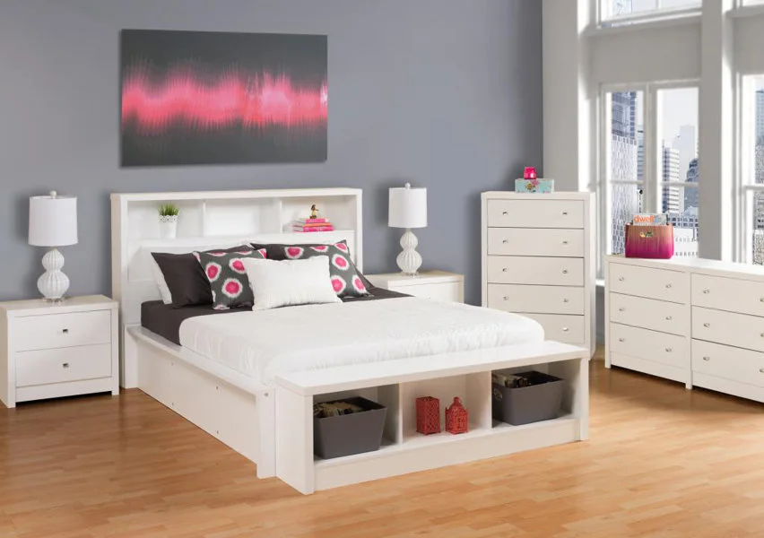 A modern bedroom with a white storage bed, matching dressers, grey walls, and a pink and grey abstract painting above the headboard.