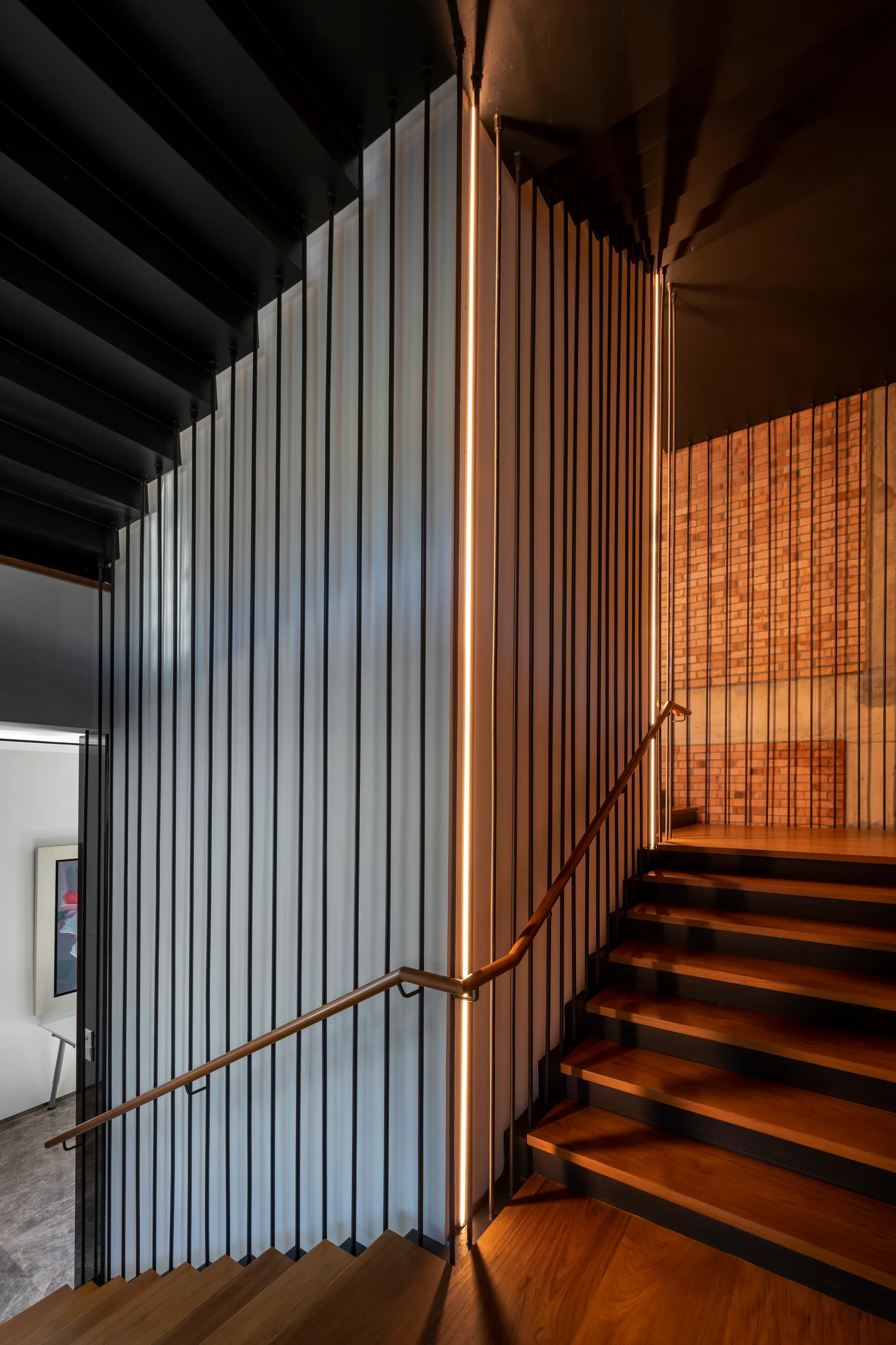 A modern wooden staircase features vertical black metal rod railings, a matching wood handrail, and a built-in vertical LED light strip.