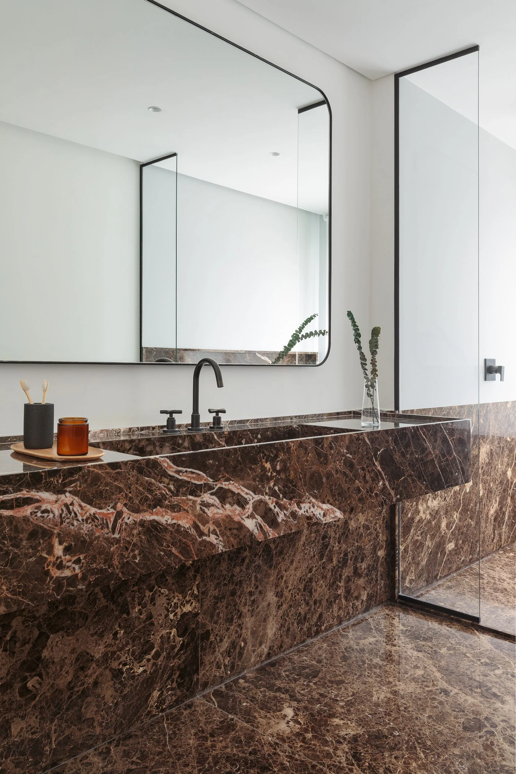 A modern bathroom featuring a polished brown marble floating vanity with an integrated sink, matching marble floor, and a thin black-framed mirror.