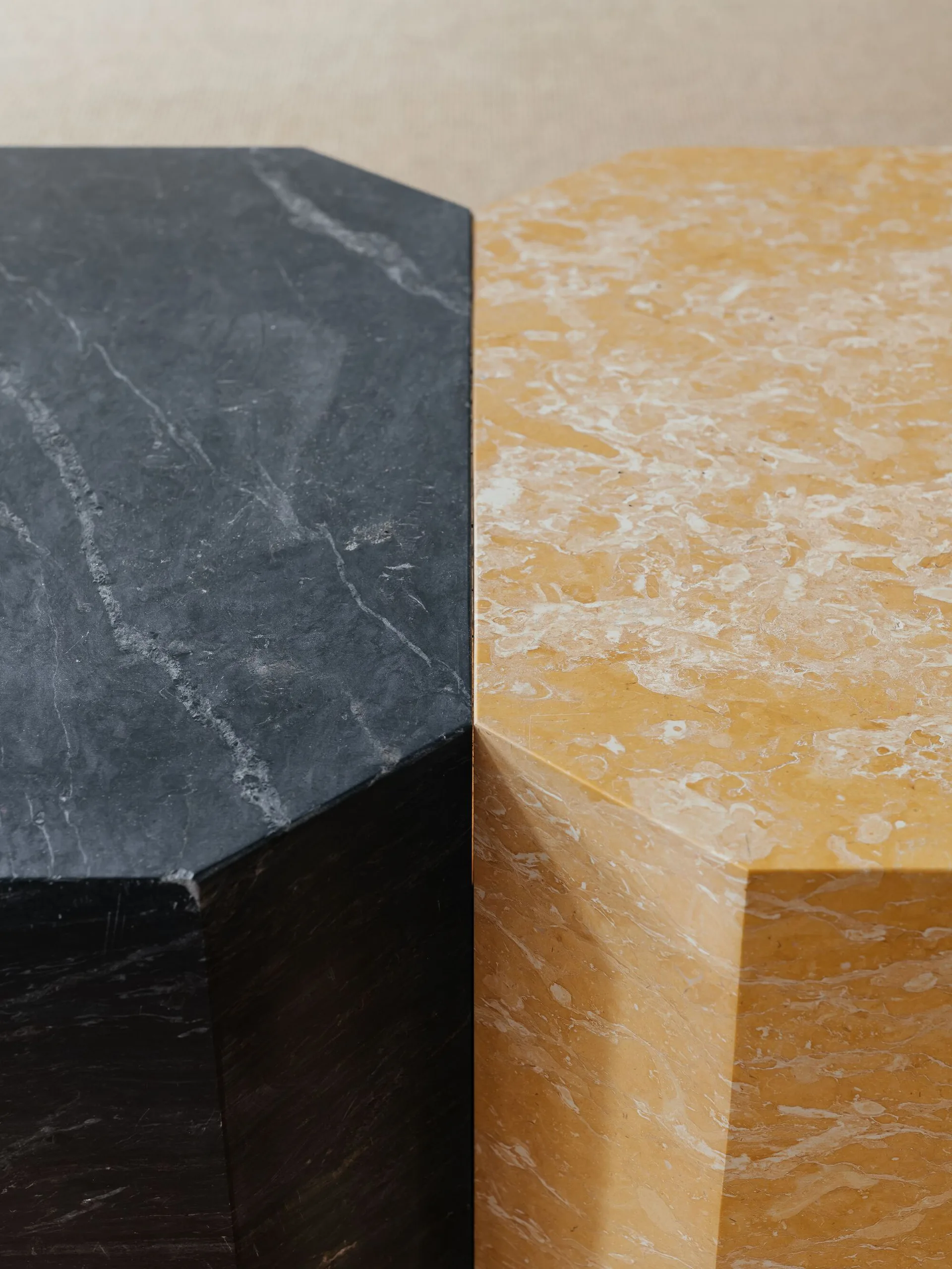 A close-up view of two geometric side tables, one crafted from black marble and the other from yellow veined marble, placed side by side.