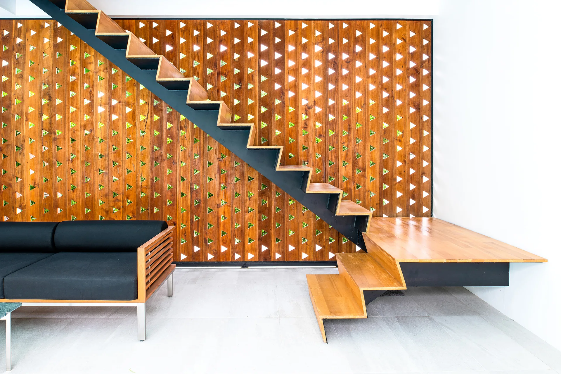 A modern staircase with wooden treads and a black metal frame is positioned against a repeating triangular wood screen wall.