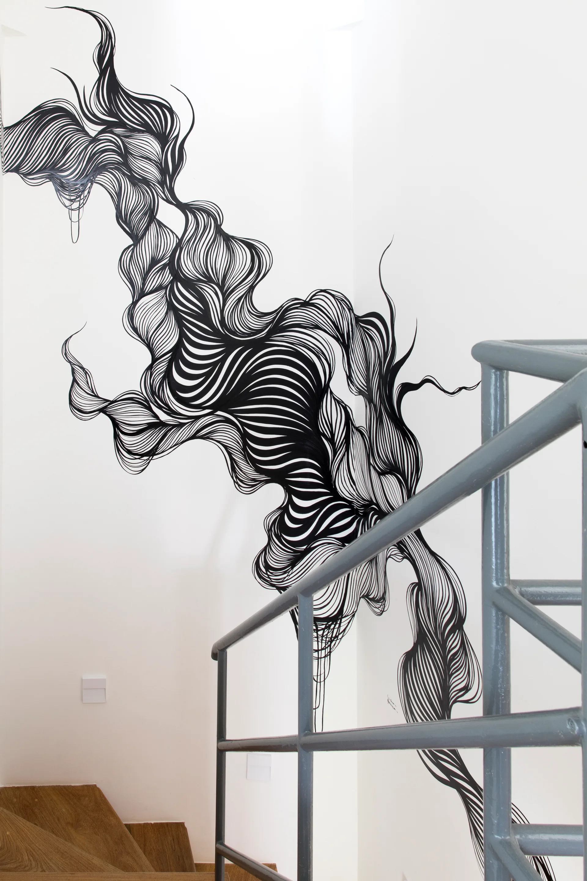A large black and white organic graphic mural covers a white wall along a staircase behind a grey metal railing.