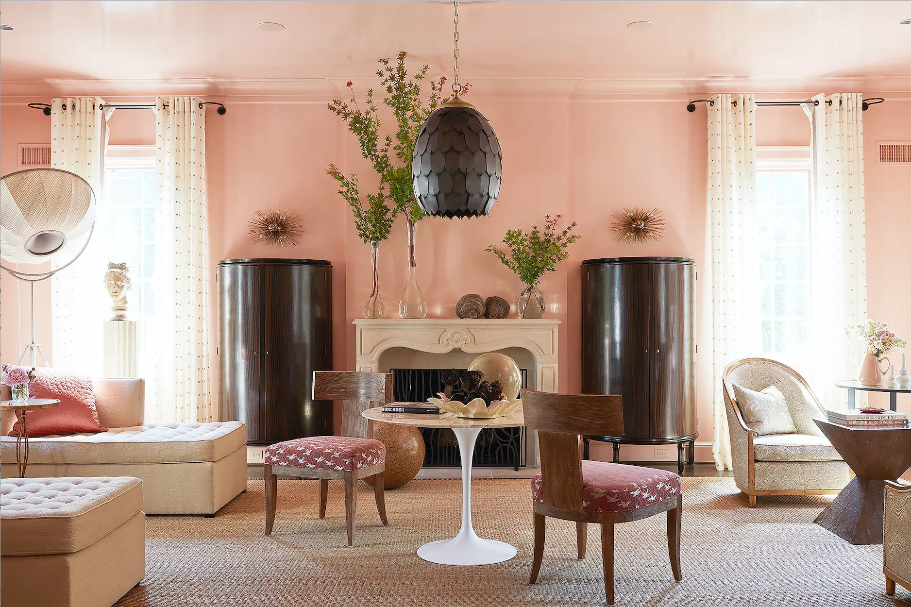 A peach-colored living room features a stone fireplace flanked by two tall dark wood cabinets, a round marble-top table, and a woven rug.