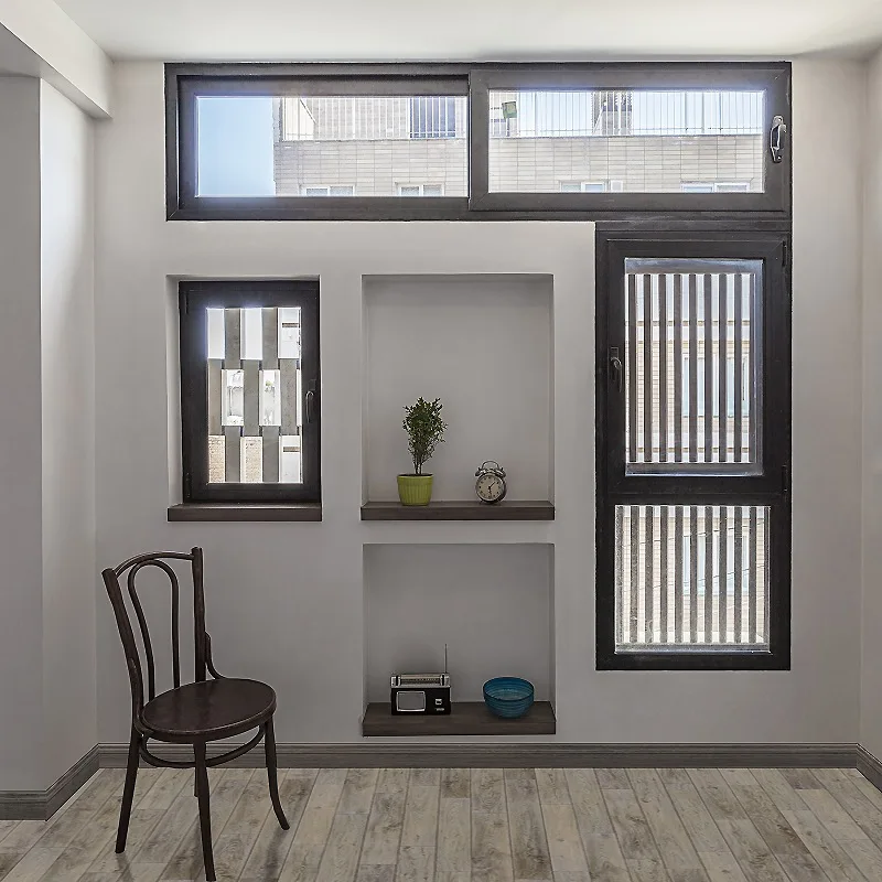 A minimalist white room corner features a dark wood bentwood chair, vertical recessed wall niches, and black-framed windows.