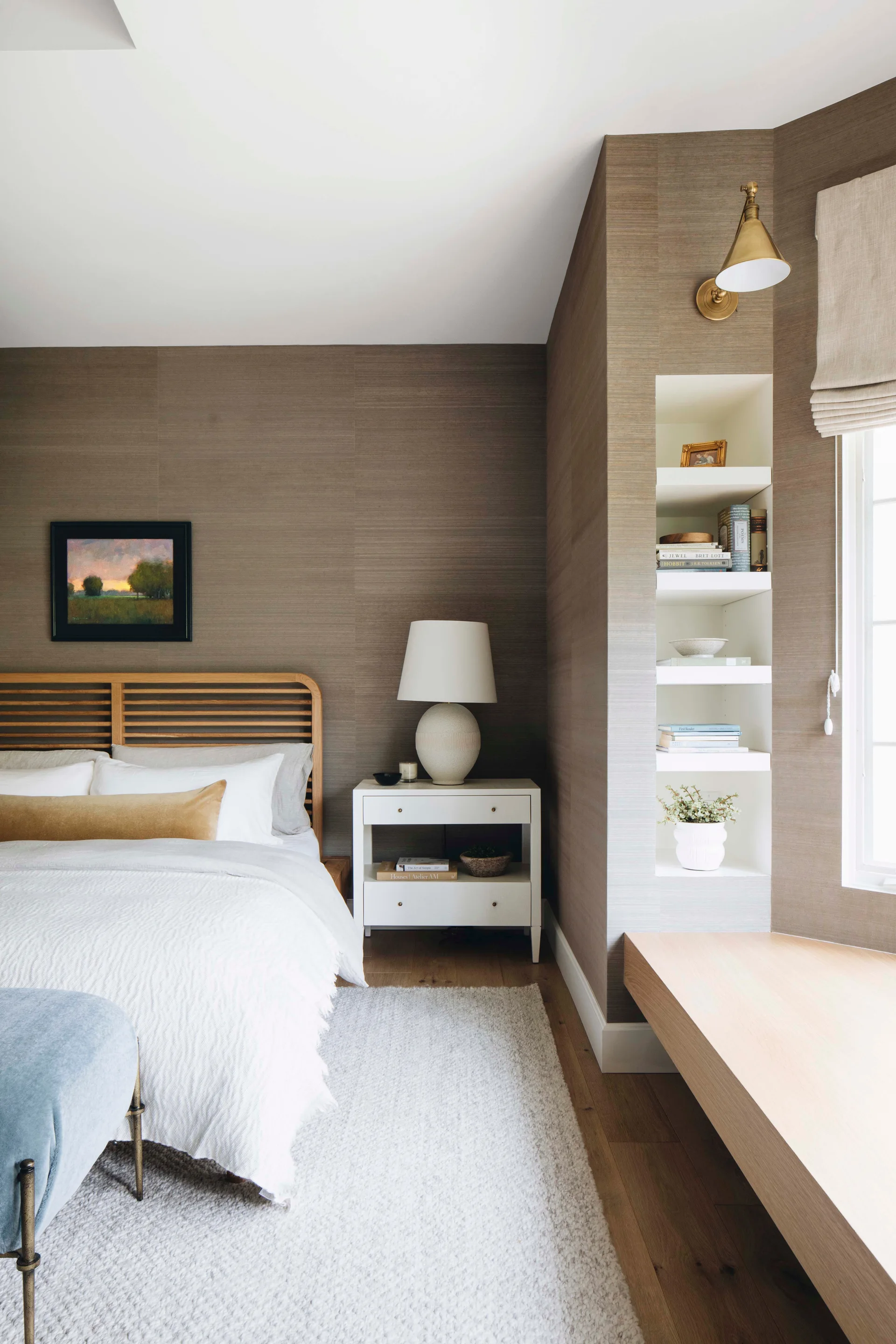 A bedroom featuring textured brown grasscloth wallpaper, a wood slatted headboard, and a white nightstand beside a recessed white shelving unit.