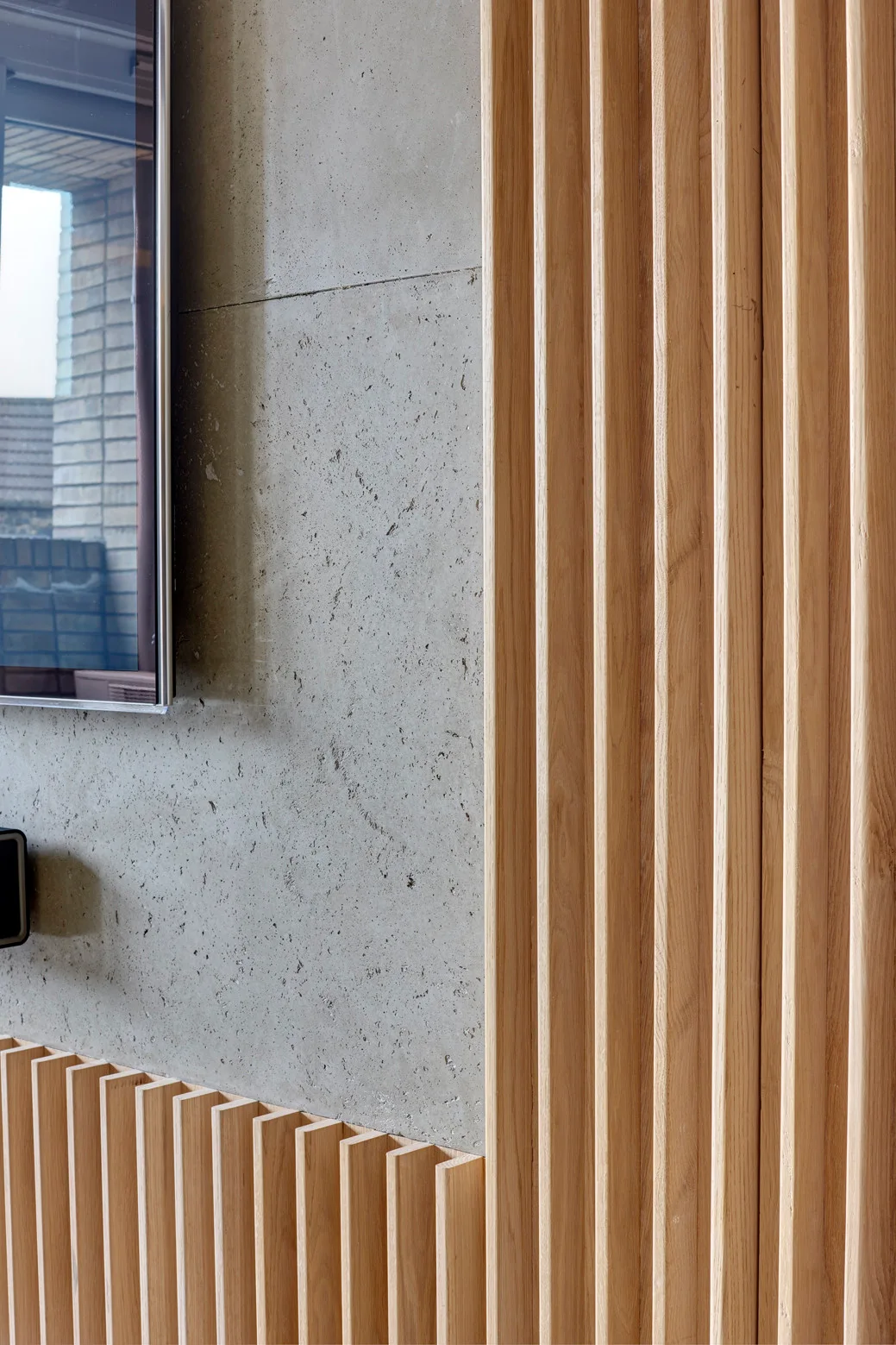 A close-up of a textured grey concrete wall accented by vertical light wood slat paneling next to a mounted flat-screen television.