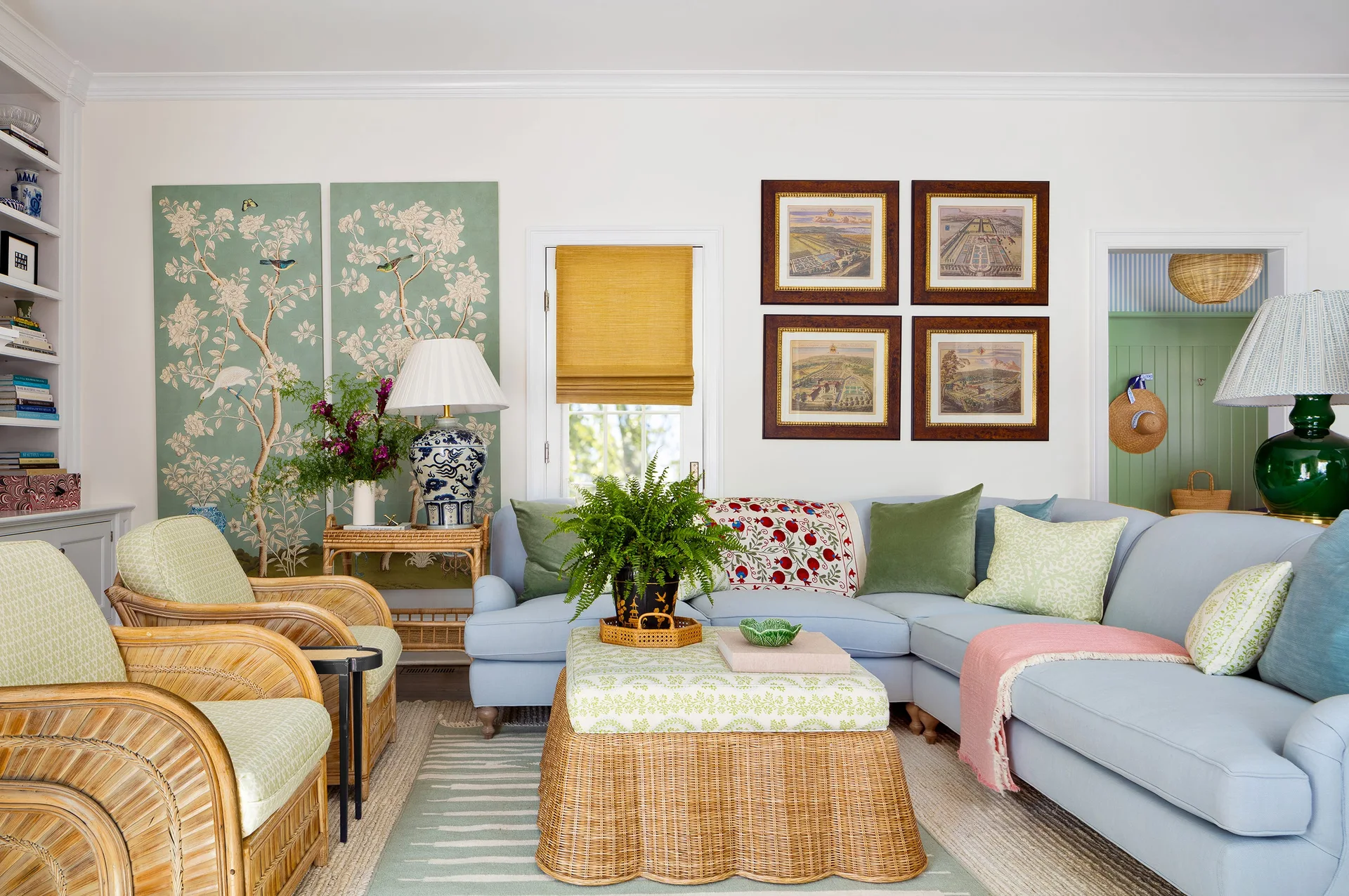 A bright living room features a blue sectional sofa, two rattan armchairs, a matching scallop-edge rattan ottoman, and green floral wall panels.
