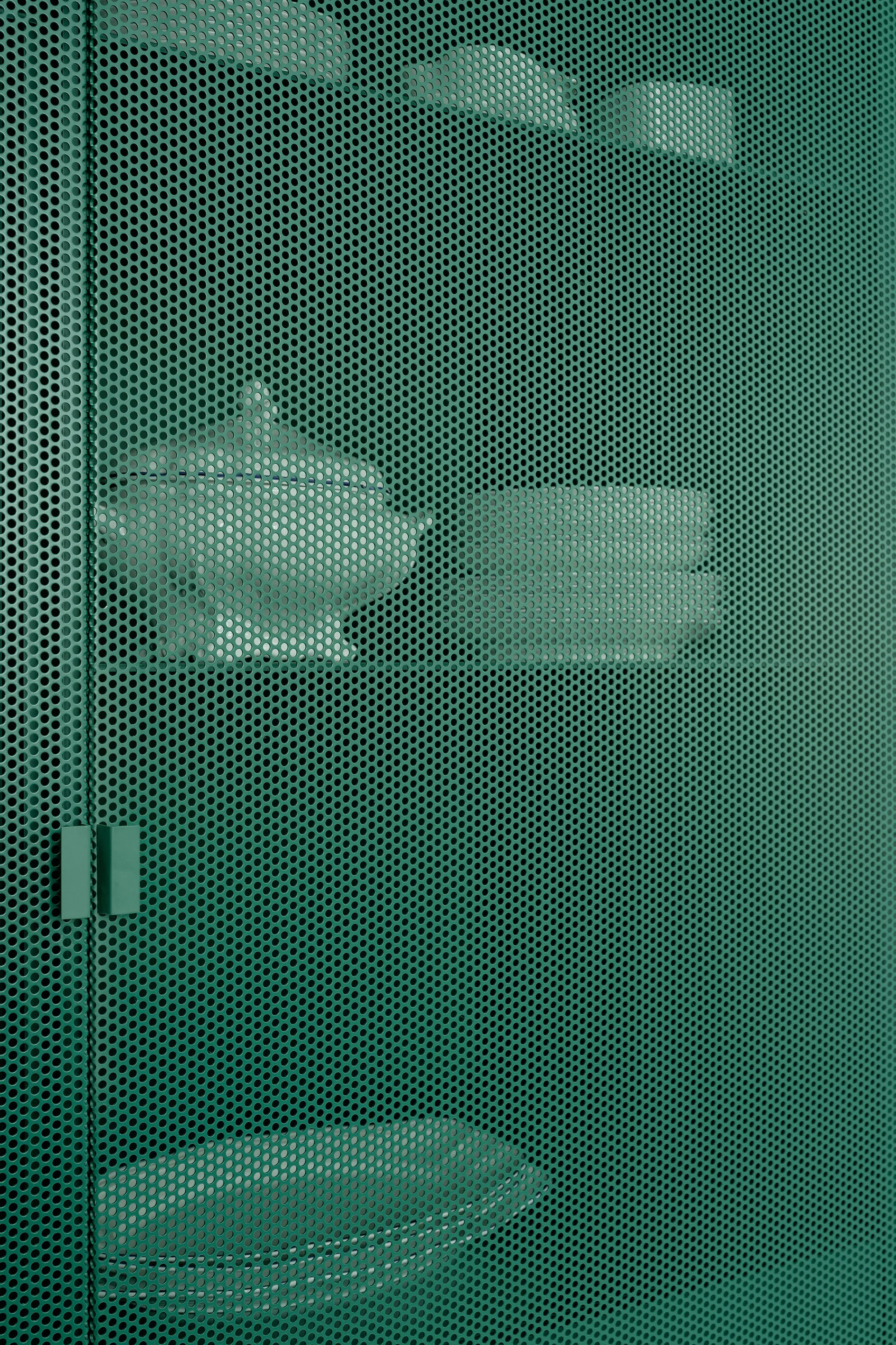 A teal green perforated metal cabinet door with small holes showing white ceramic tableware stored on shelves inside.