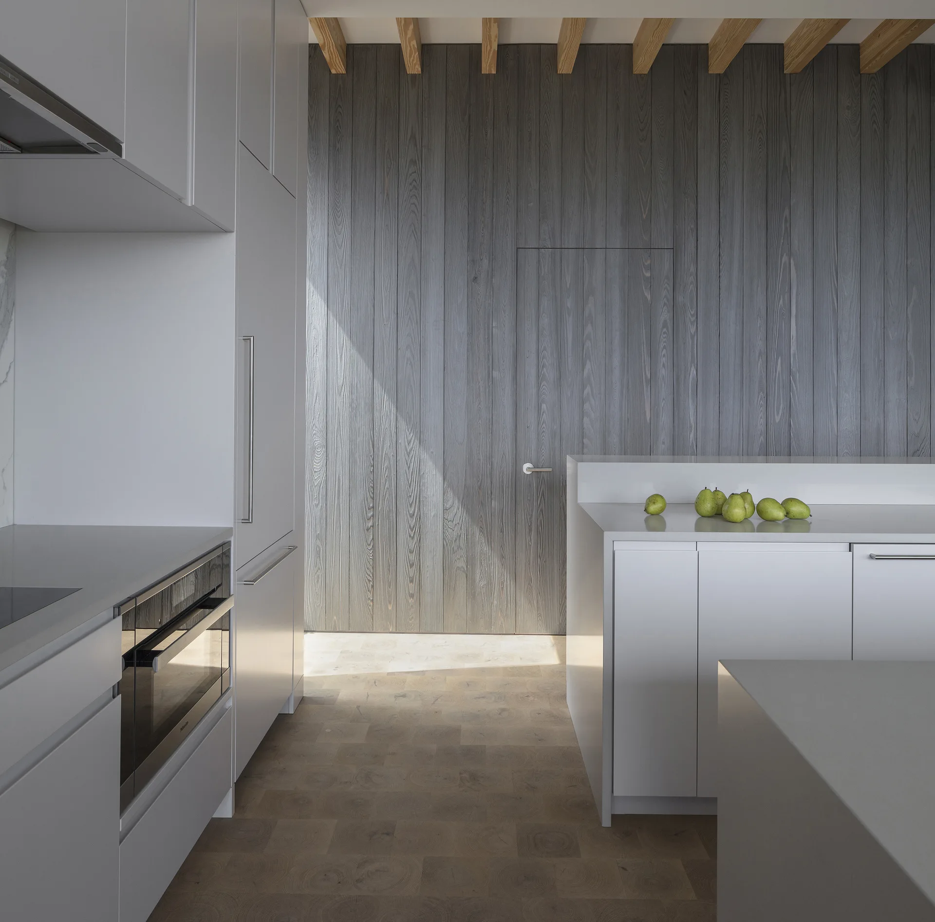 A minimalist kitchen featuring matte white cabinets, an island, and a vertical grey wood-paneled wall with a flush integrated door.
