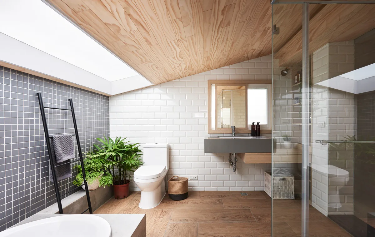 A modern bathroom features a sloped wood ceiling with a skylight, white subway tiles on the walls, a white toilet, and a glass shower.