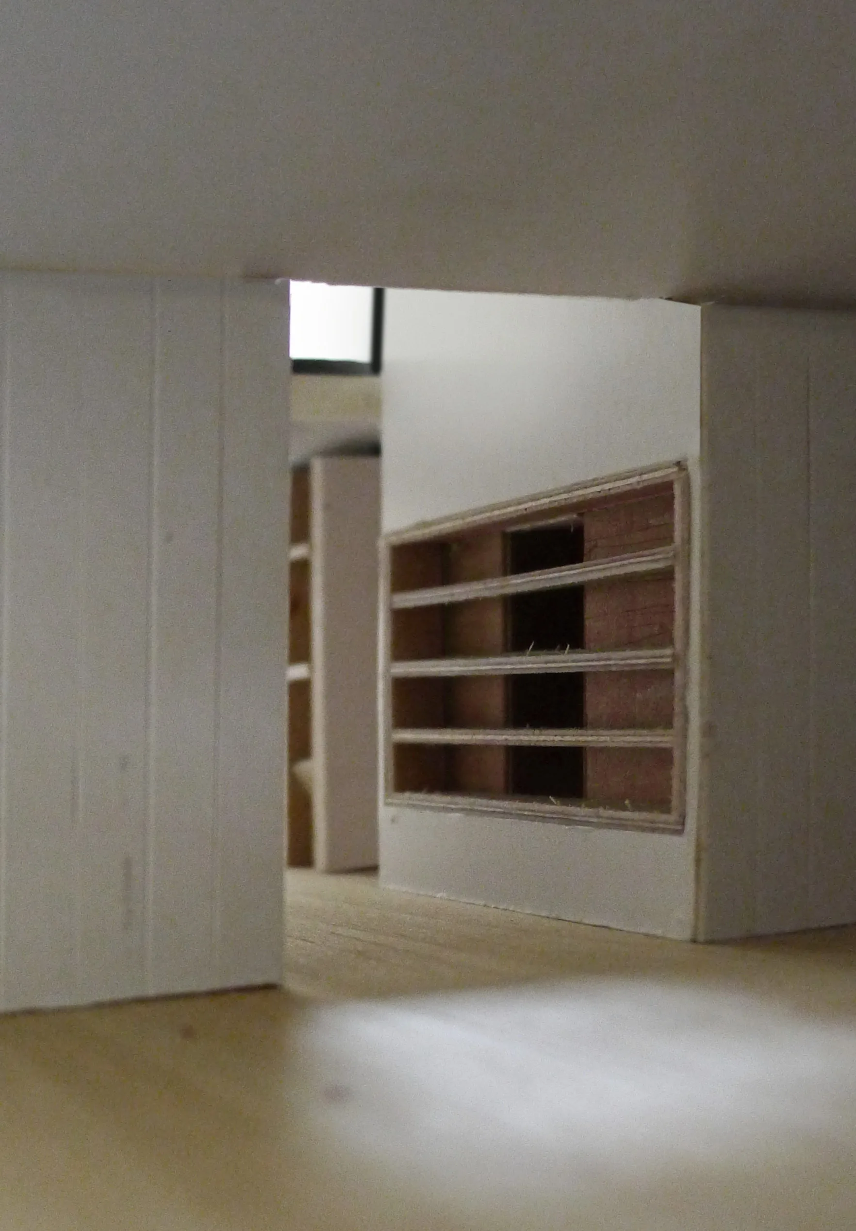 An architectural scale model features white partition walls, an open passage, and miniature recessed wooden shelving.
