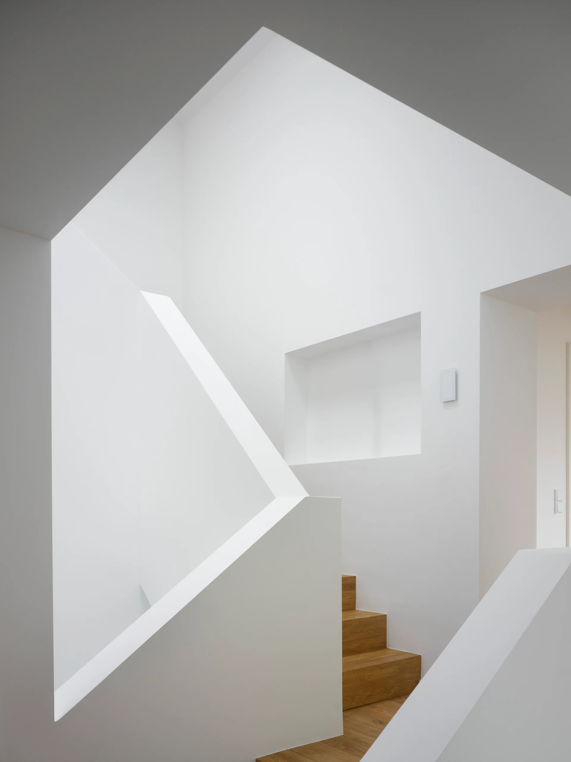 A minimalist modern staircase featuring wood steps set between solid white geometric walls with a recessed square niche.