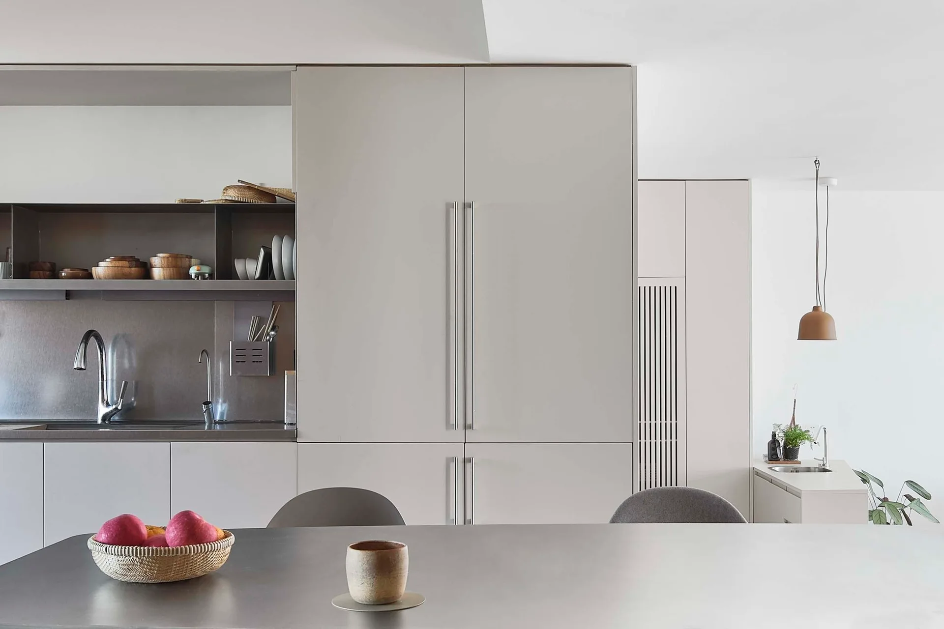 A modern minimalist kitchen featuring matte pale grey floor-to-ceiling cabinets, a stainless steel backsplash alcove, and a smooth grey island.