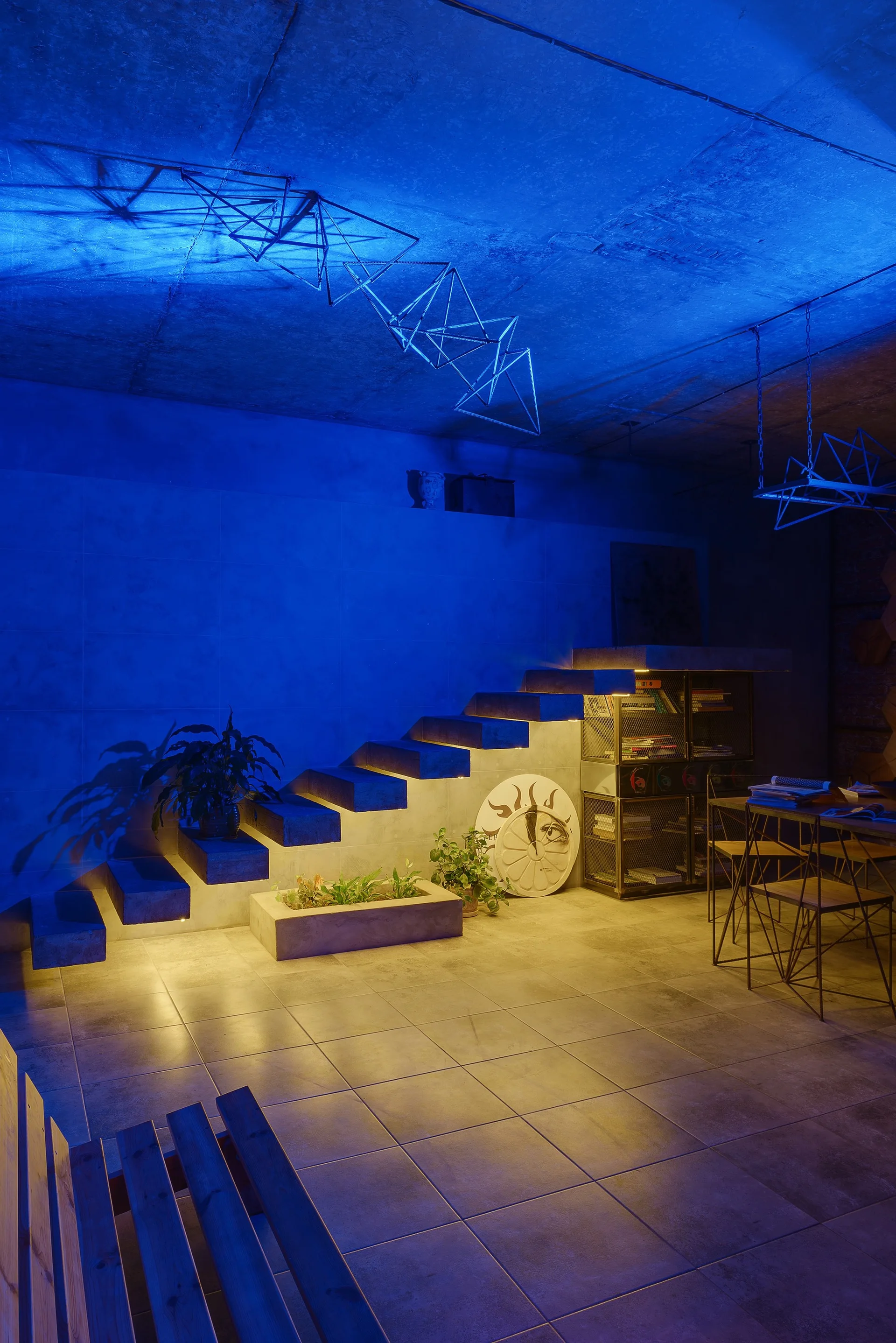 Floating concrete stairs lit by glowing yellow under-step lights ascend along a wall washed in dramatic blue light.
