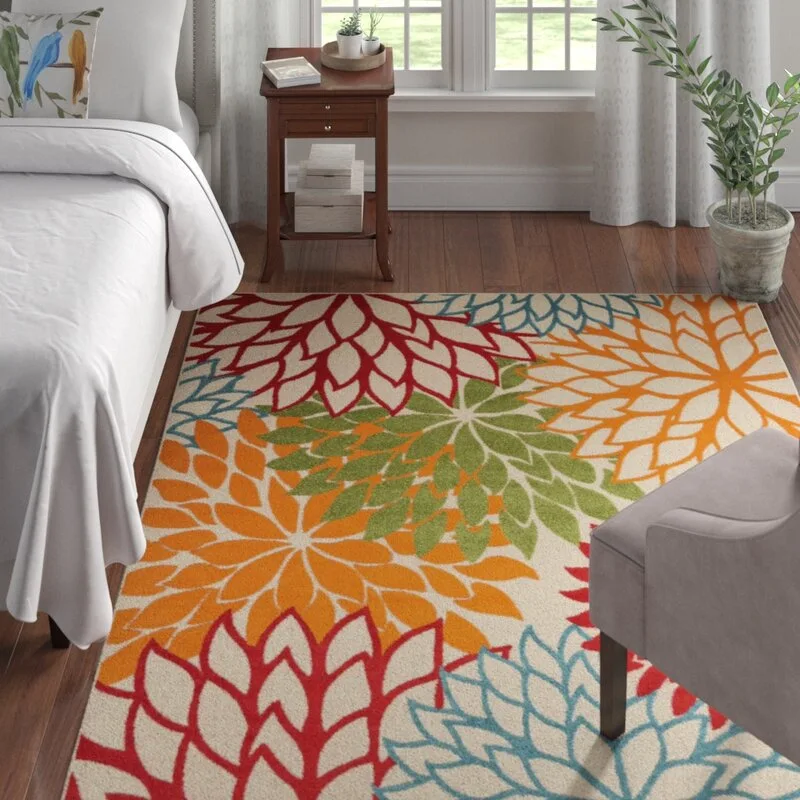 A colorful floral-patterned area rug lies on a dark wood floor in a bedroom next to a white bed and a wooden nightstand.