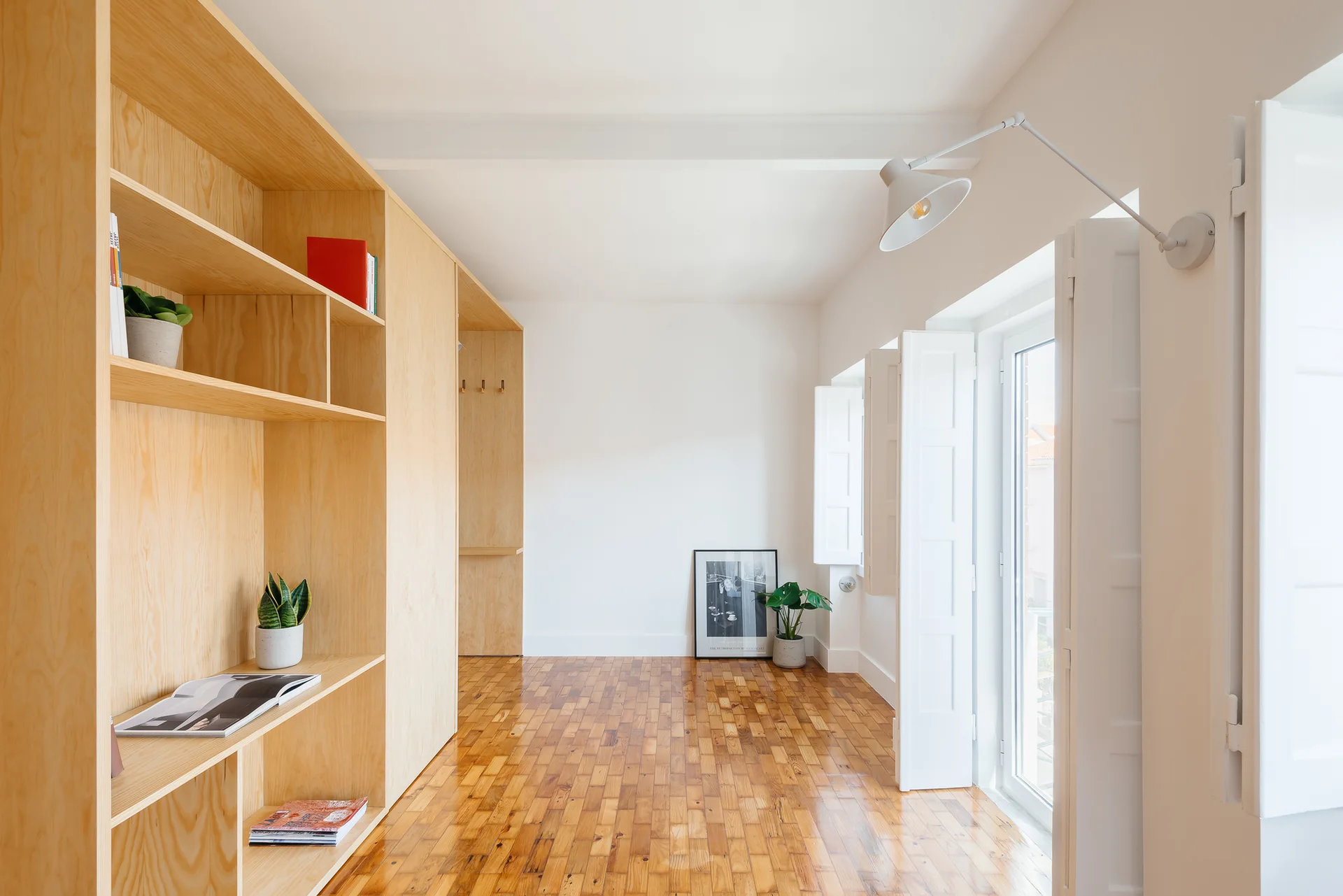A minimalist entryway with light wood plywood built-in cabinets, a parquet wood floor, and white walls with an articulated wall lamp.