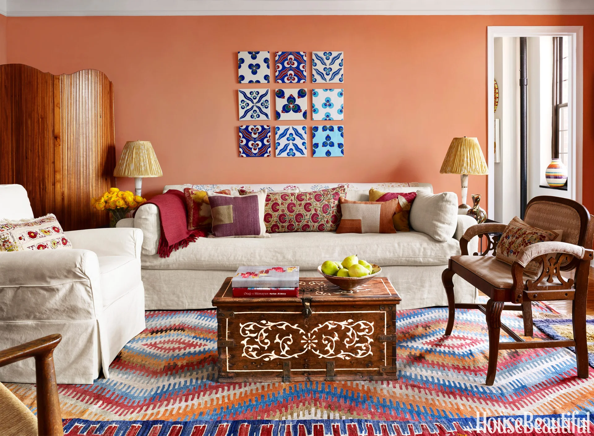 An apricot living room features a cream sofa, a grid of nine patterned blue ceramic tiles on the wall, and an antique wooden chest as a coffee table.