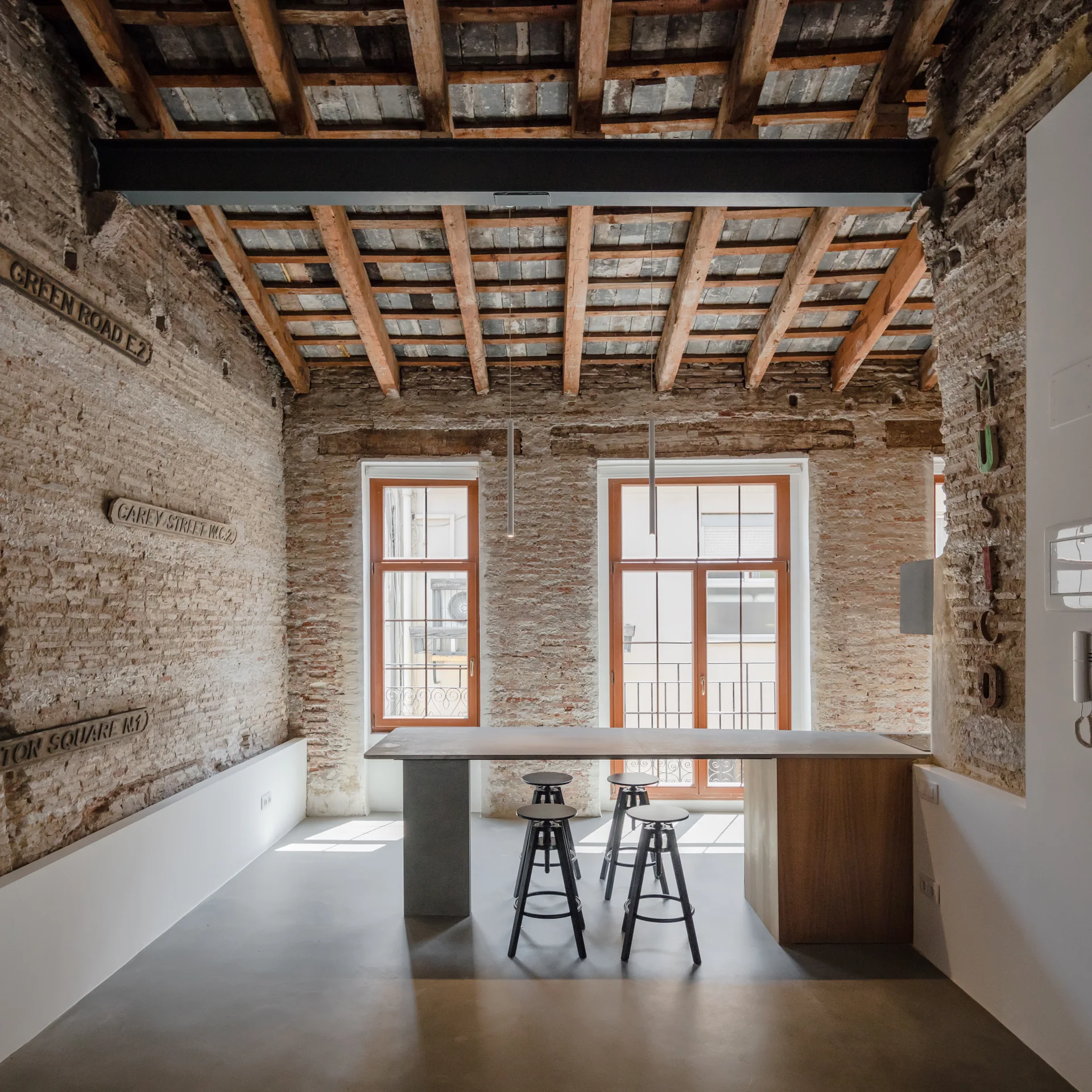An industrial dining area features textured brick walls, a wood plank ceiling with exposed beams, and a long kitchen island with black metal stools.