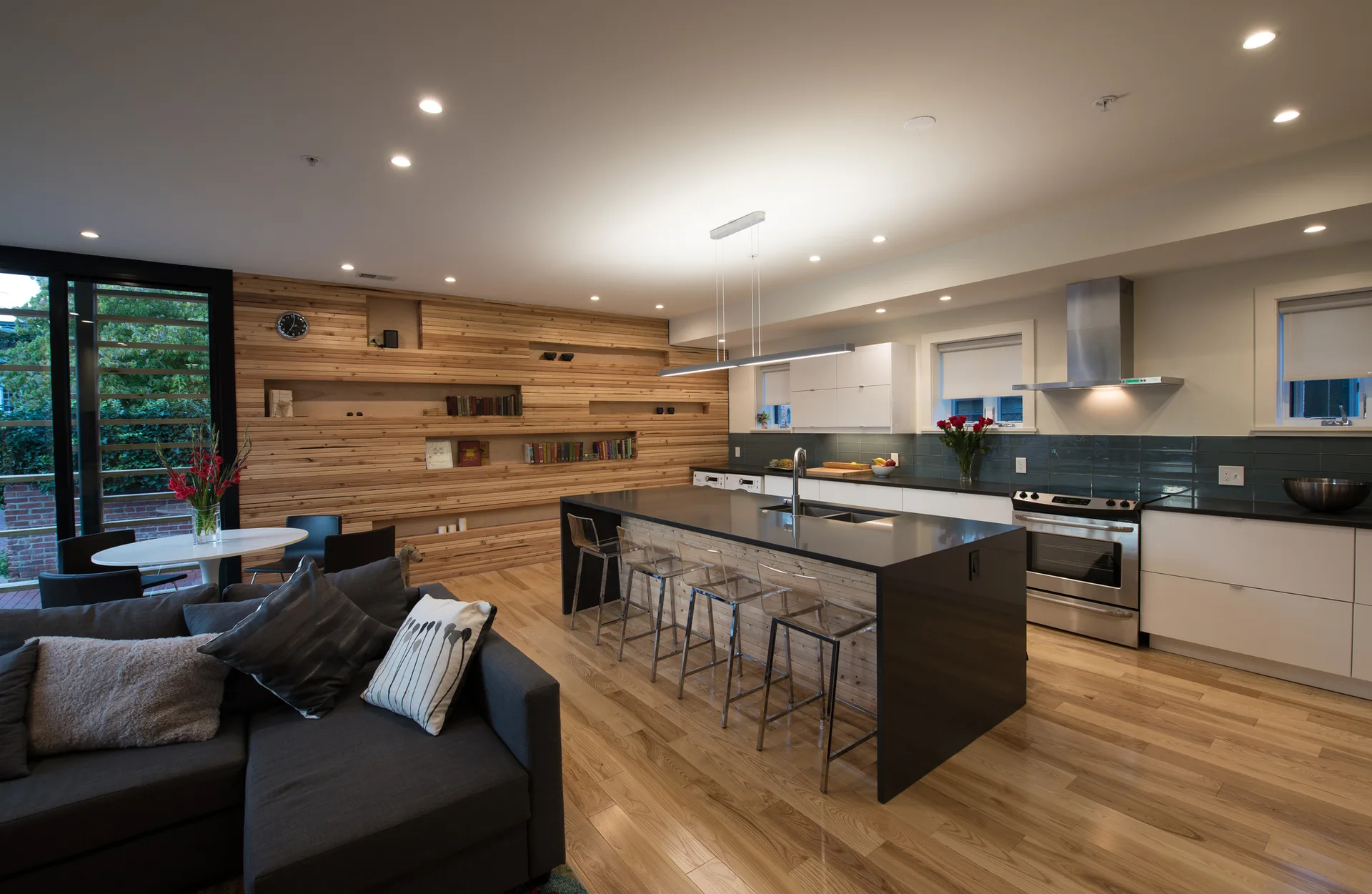A contemporary open-concept kitchen features a large dark island with clear acrylic stools, set against a horizontal wood slat accent wall.