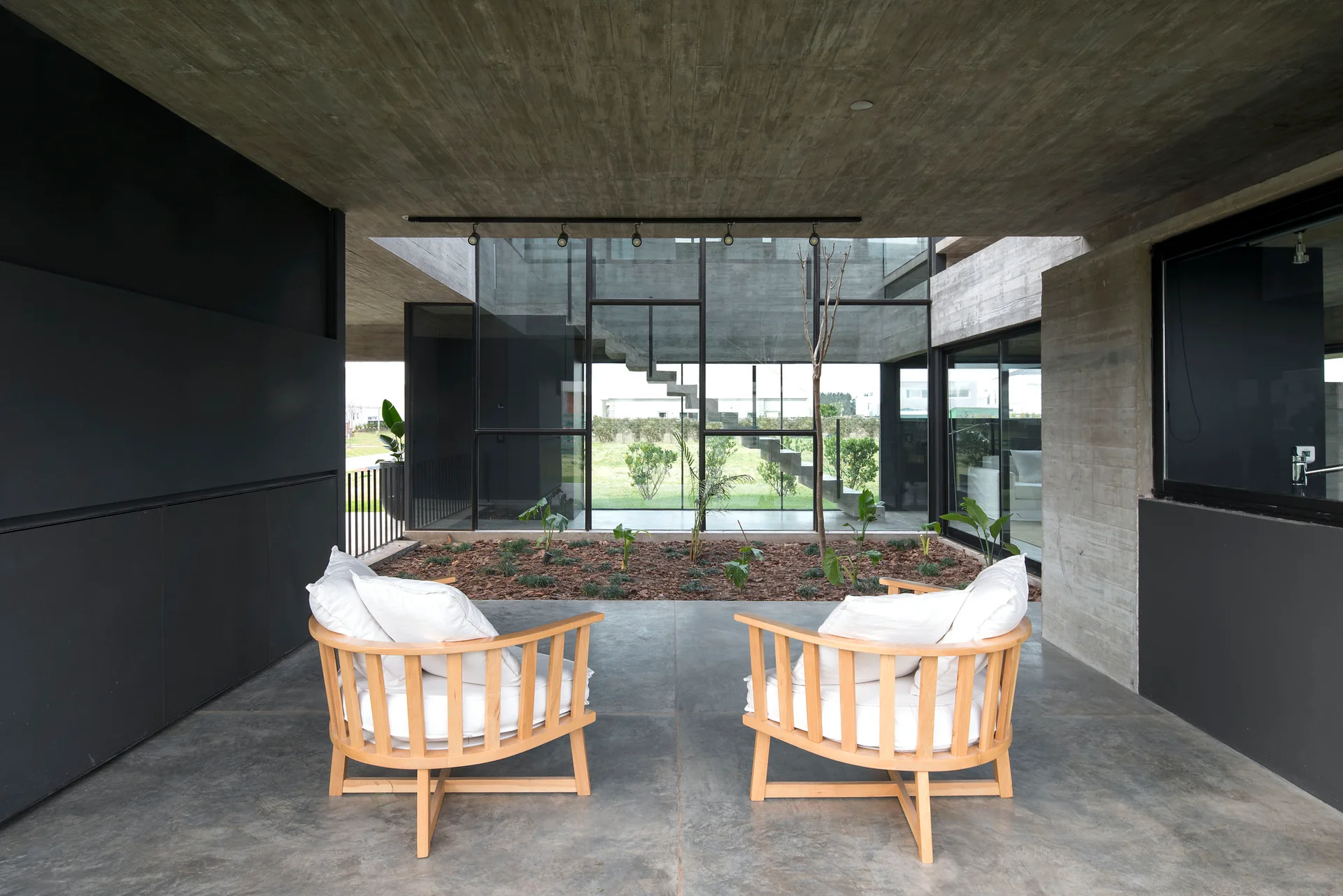 Two rounded light wood armchairs with white cushions face an open-air central courtyard on a modern concrete patio.
