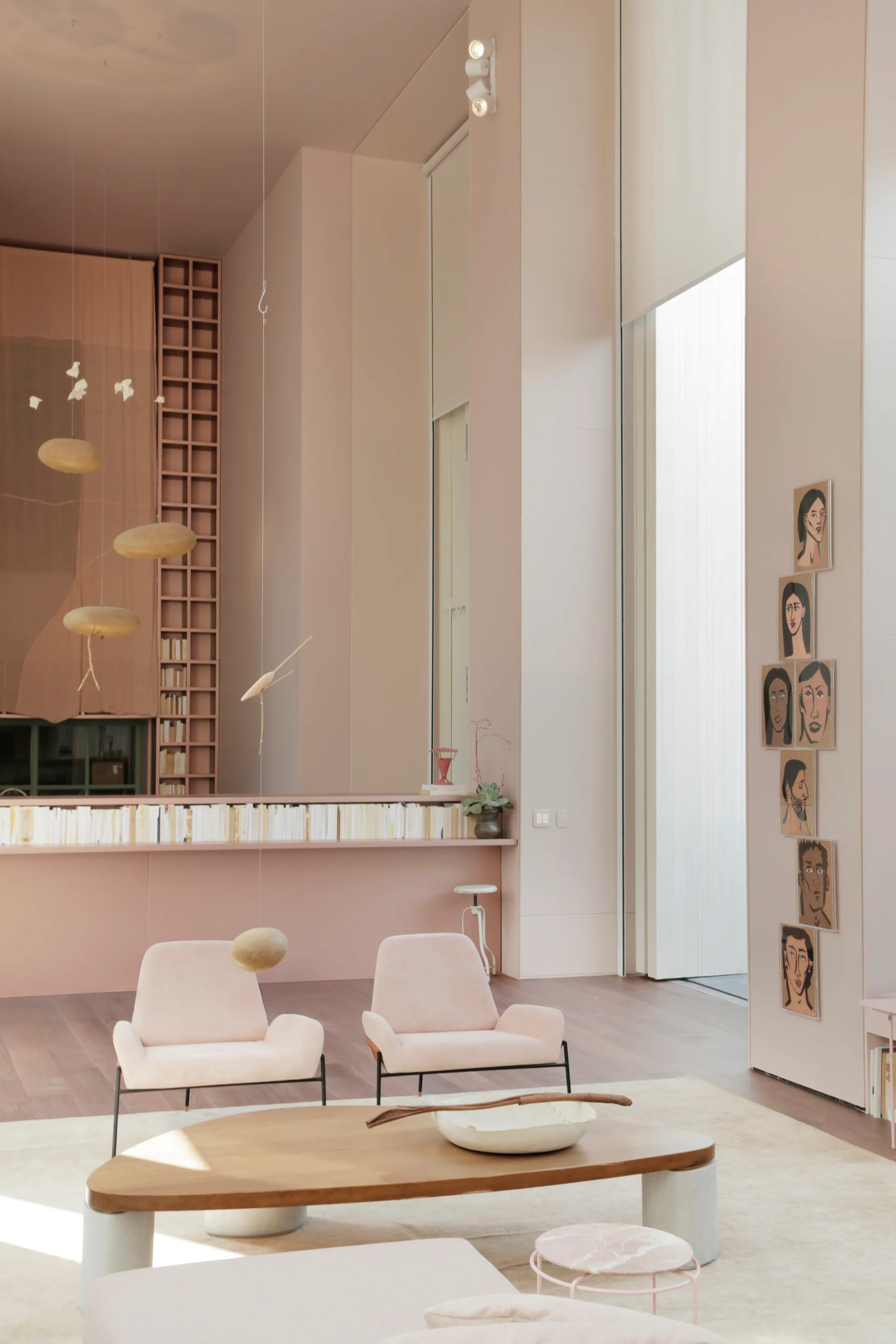 A high-ceilinged living room with monochromatic pink walls and ceiling features two pale pink armchairs and a low wooden coffee table on a cream rug.