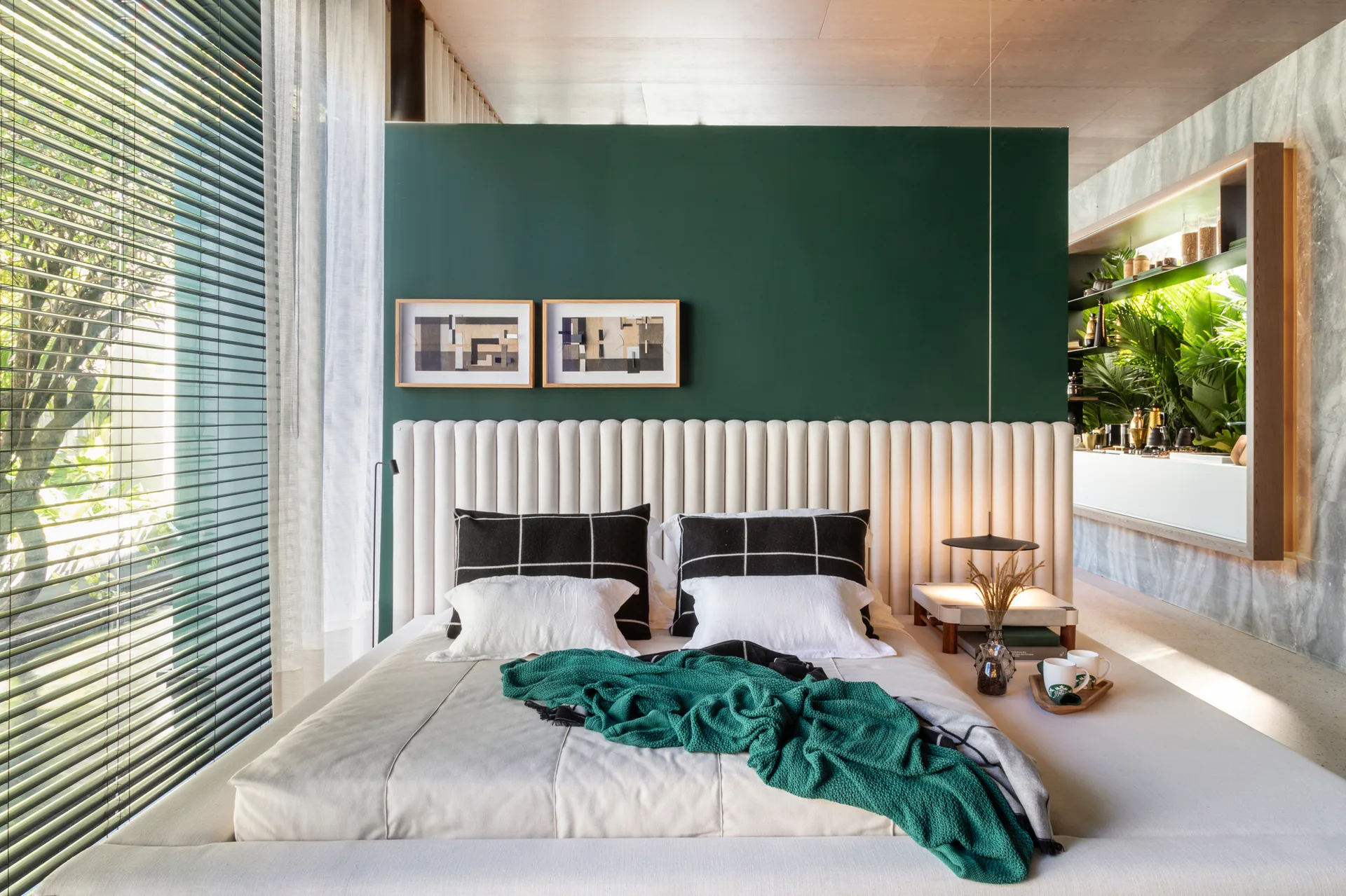 A modern bedroom features a cream channel-tufted headboard against a dark green wall, styled with black and white pillows and a green throw blanket.