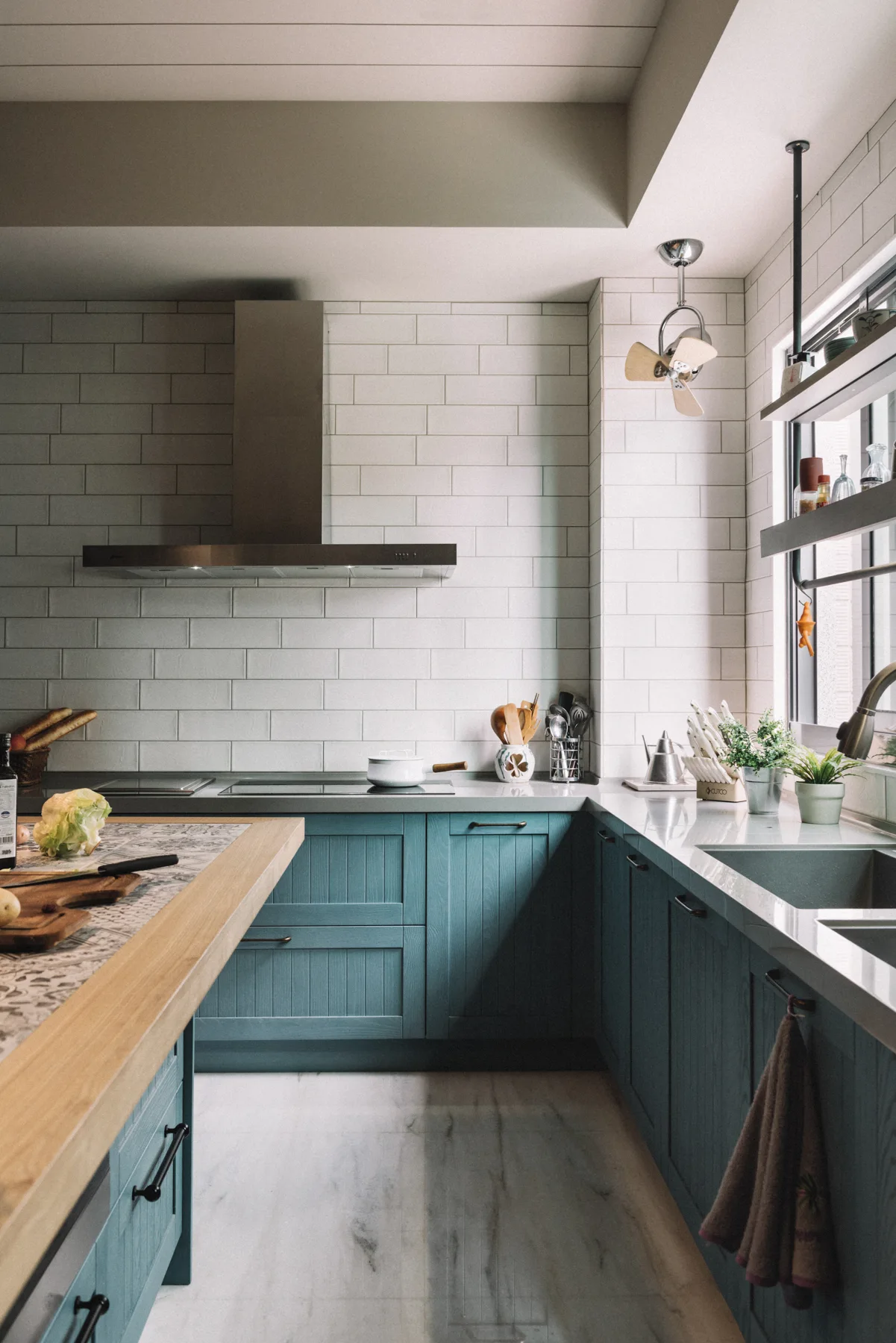 A kitchen featuring blue shaker cabinets, white subway tile backsplash, and a central island with a wood-framed tiled countertop.