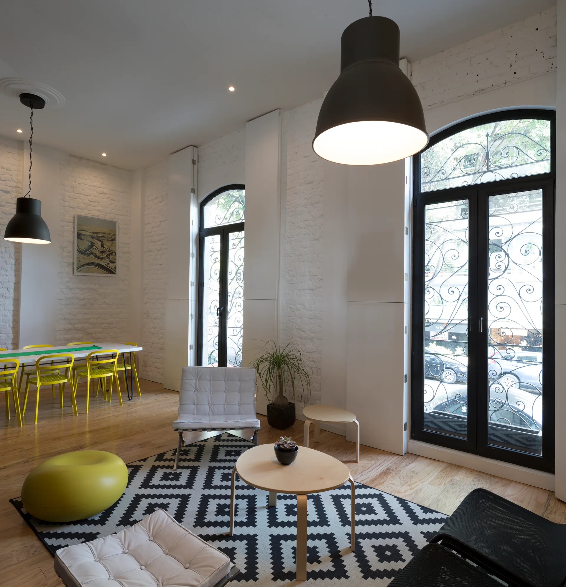 A light-filled living area features white painted brick walls, two large arched windows with black frames, and a black-and-white geometric rug.