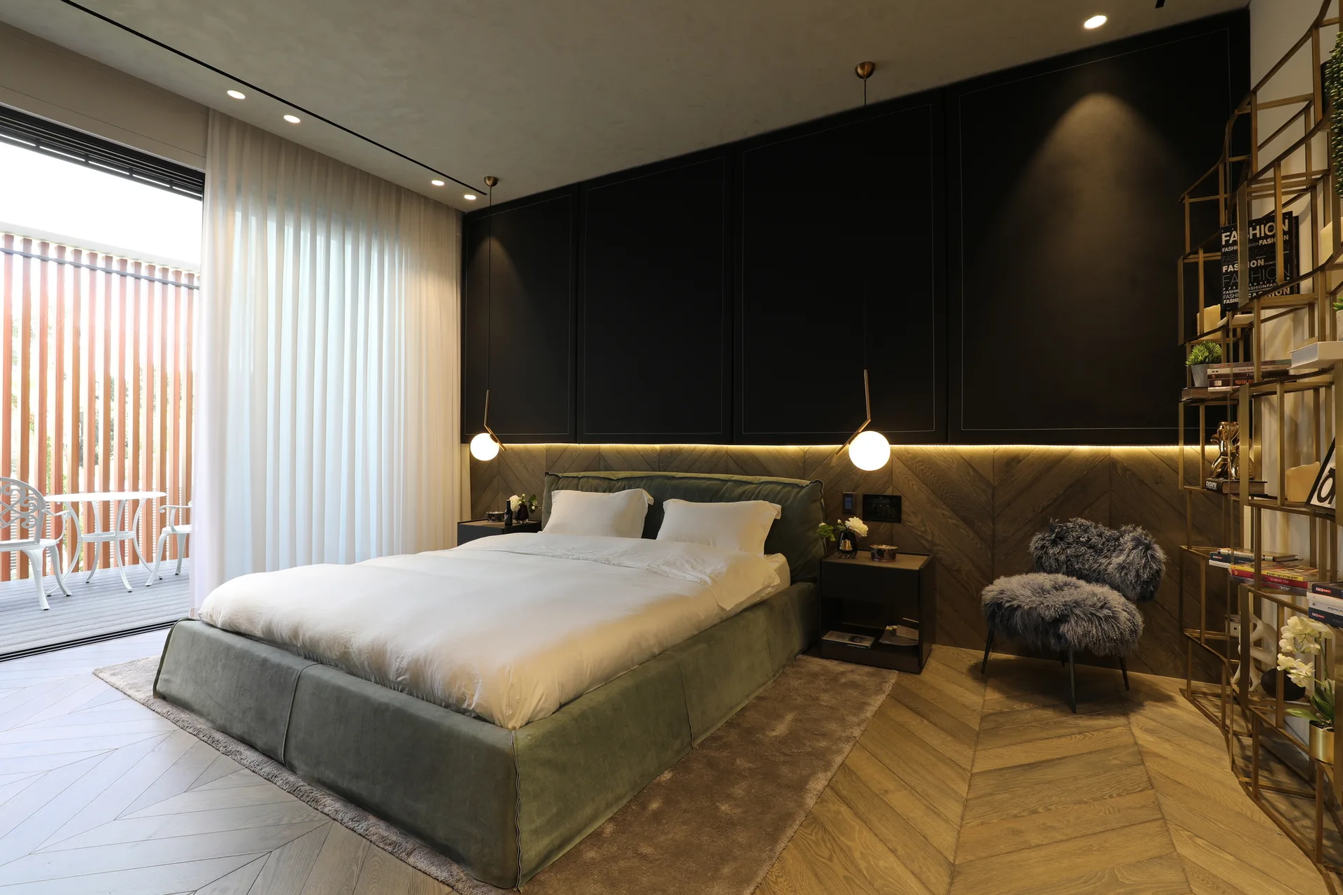 A modern bedroom featuring a green upholstered bed, a black and wood-paneled feature wall with LED lighting, and chevron wood flooring.