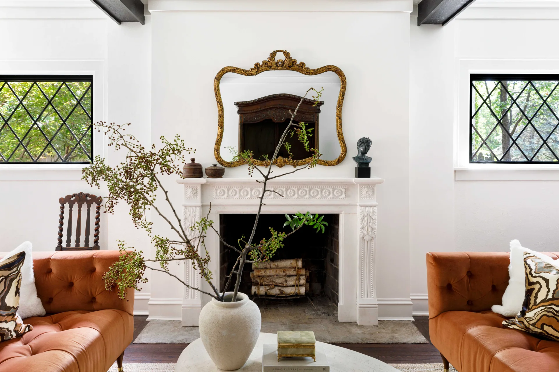 A symmetrical living room features a white ornate fireplace flanked by two orange tufted sofas, with a gold mirror hanging above the mantel.