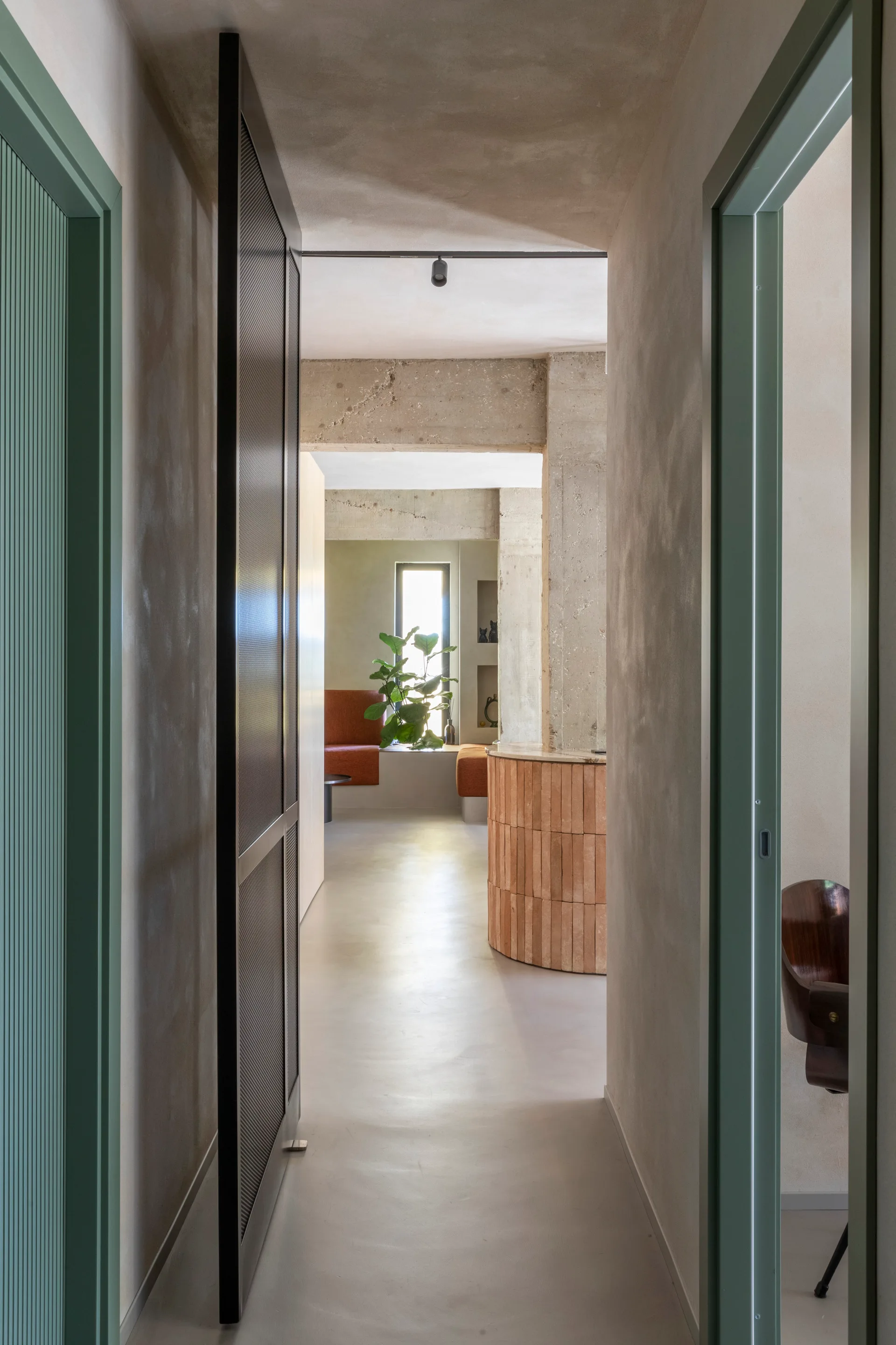A view down a smooth plaster hallway with green door frames leads to an open room featuring an exposed concrete pillar and curved tiled island.