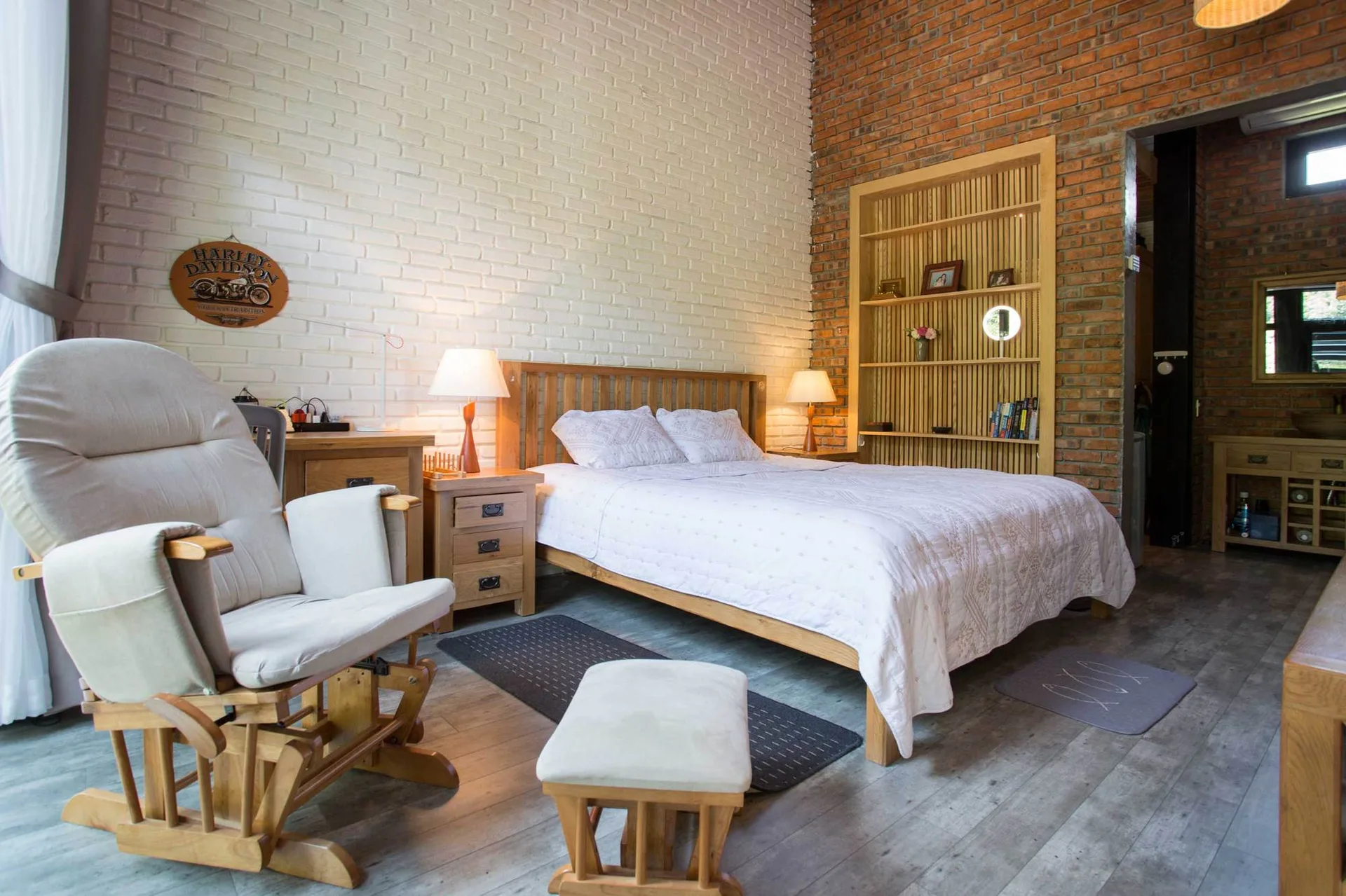 A rustic bedroom features a wooden bed set against a white painted brick wall, adjacent to an exposed red brick wall with built-in slatted shelving.