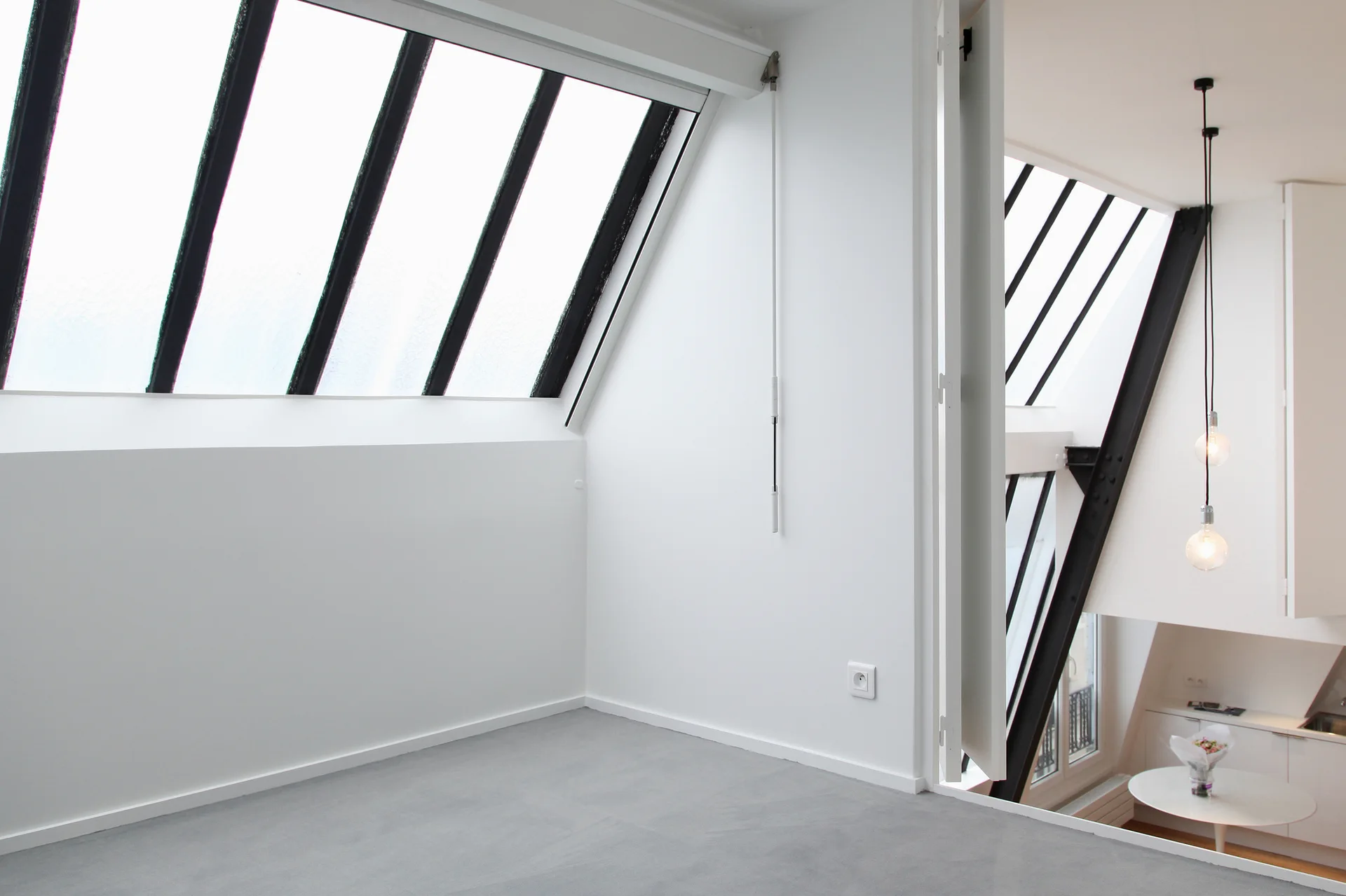 A minimalist white loft mezzanine features a smooth grey floor and large sloped skylight windows looking down to a lower level.