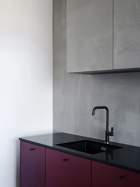 Modern kitchen featuring deep purple lower cabinets, a black countertop with a sink, and a grey concrete-effect backsplash.