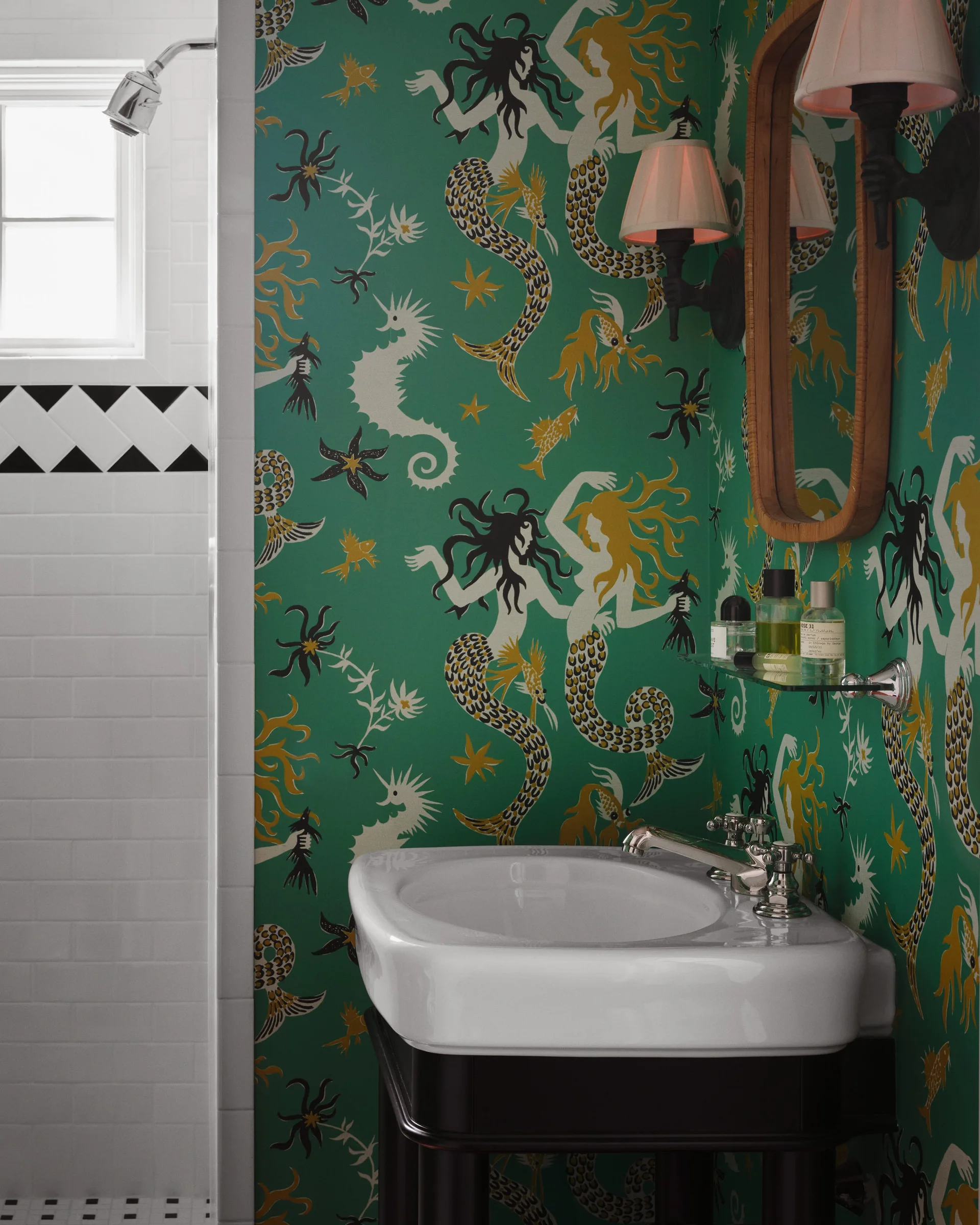 A green bathroom features whimsical mermaid-patterned wallpaper, a white pedestal sink with a chrome faucet, and white subway tile with black accent trim.