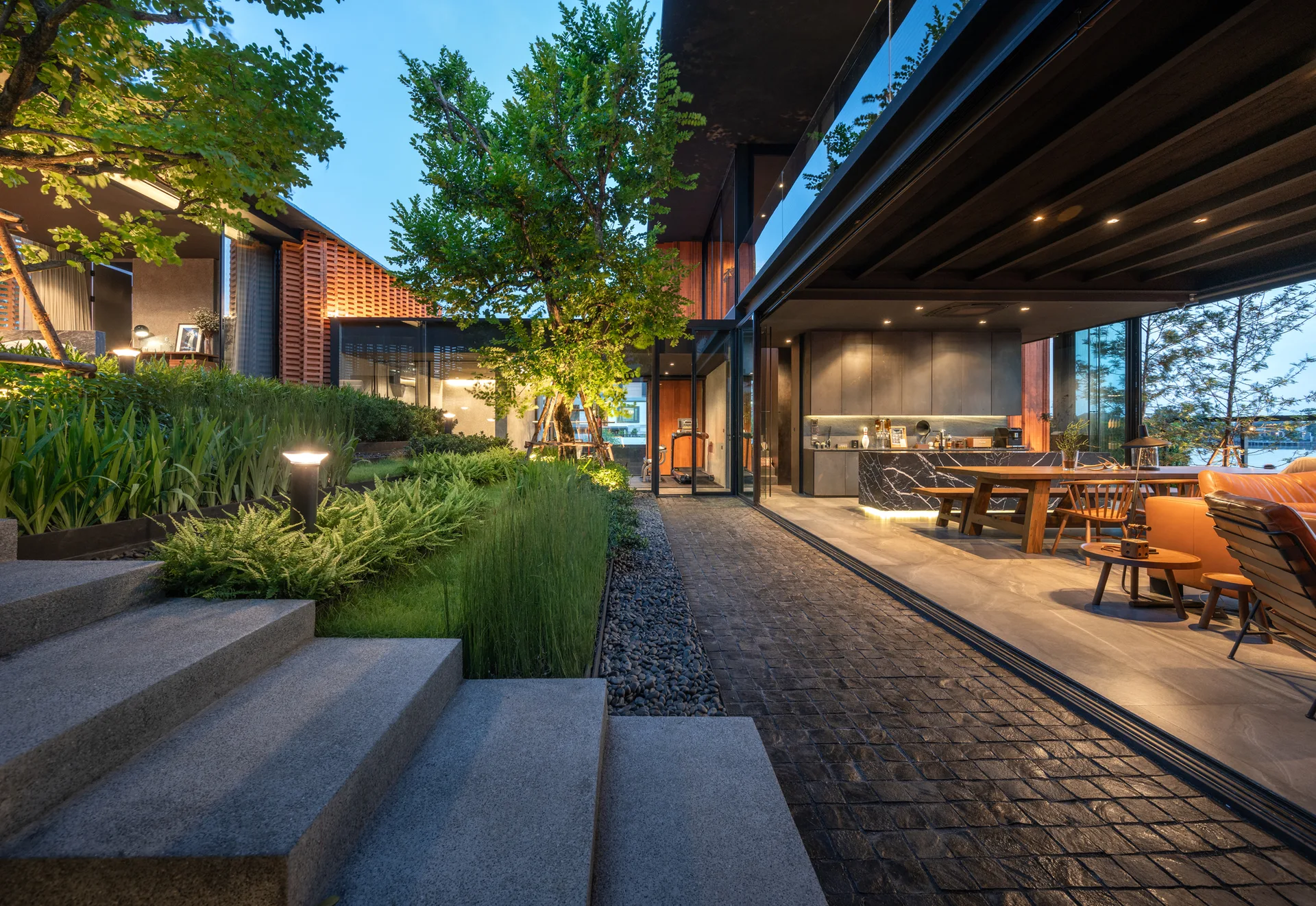 A modern open-concept kitchen and lounge with retractable glass doors opening onto a landscaped patio with stone steps and garden.