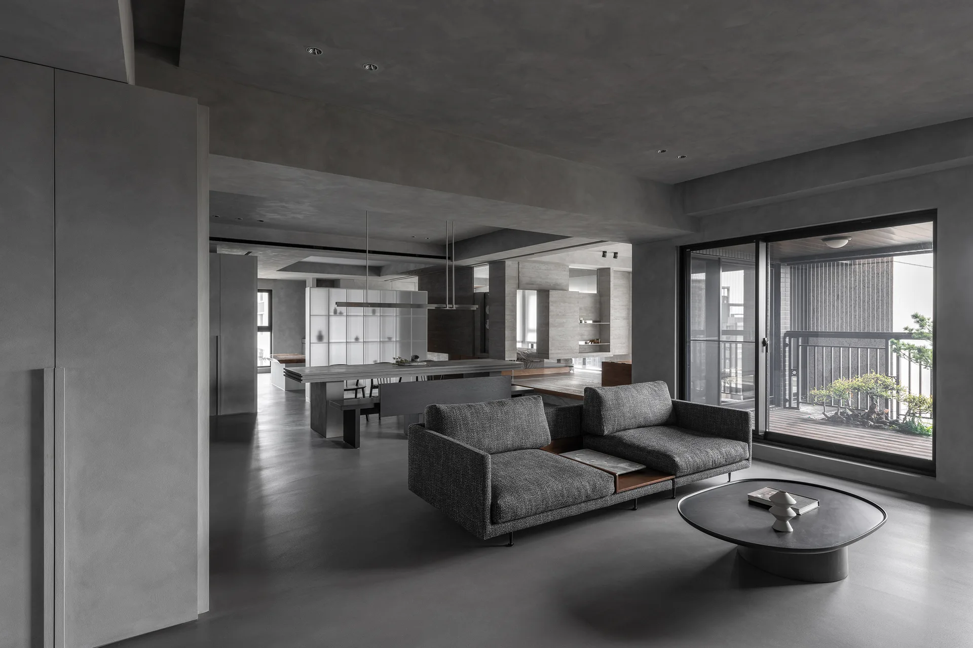 A modern grey open-plan apartment featuring a low-profile sofa, a metal coffee table, and a concrete-like matte finish on the walls.