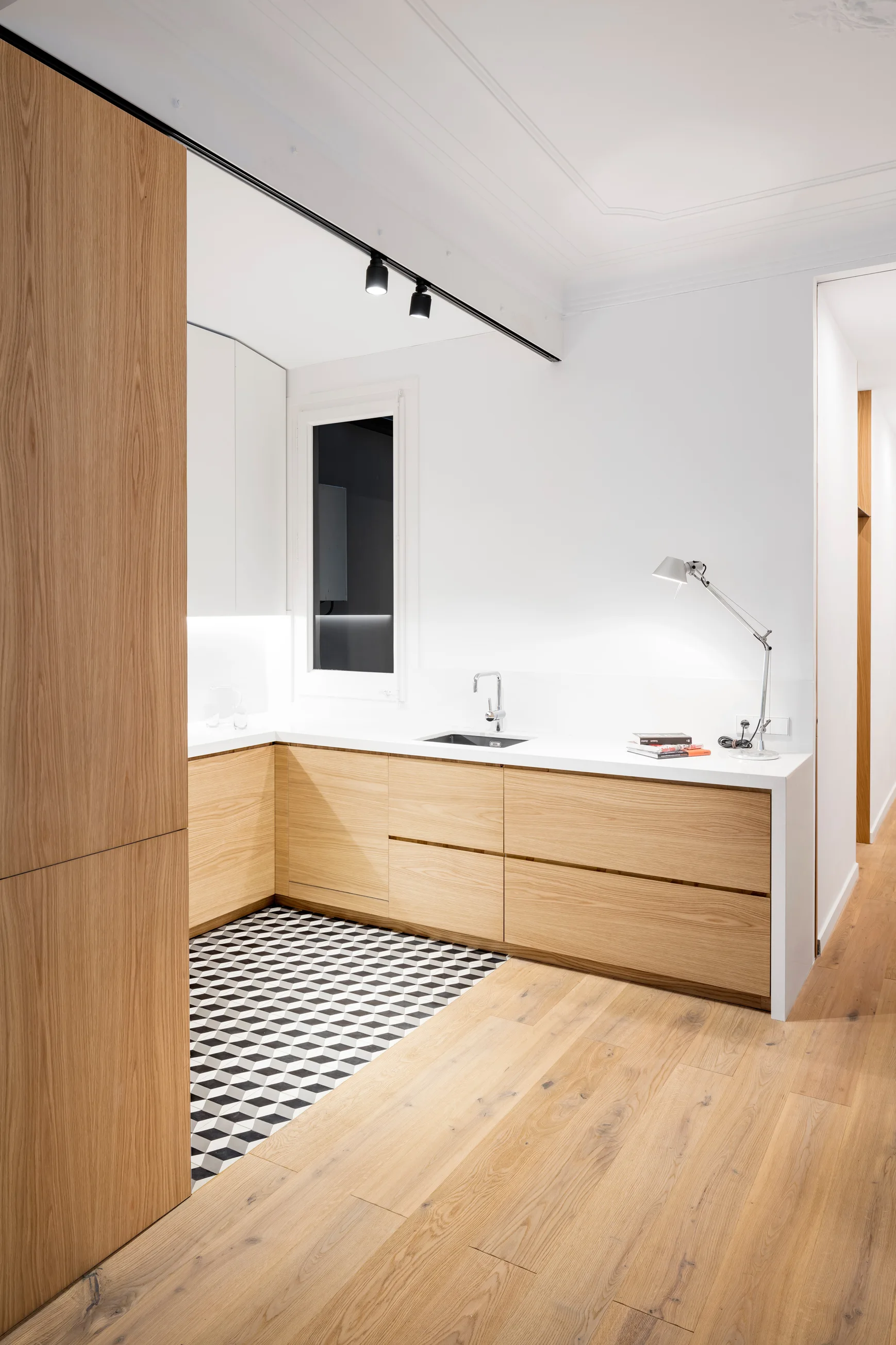 A modern kitchen with light wood lower cabinets, a white countertop, and a black and white geometric cube-patterned floor.