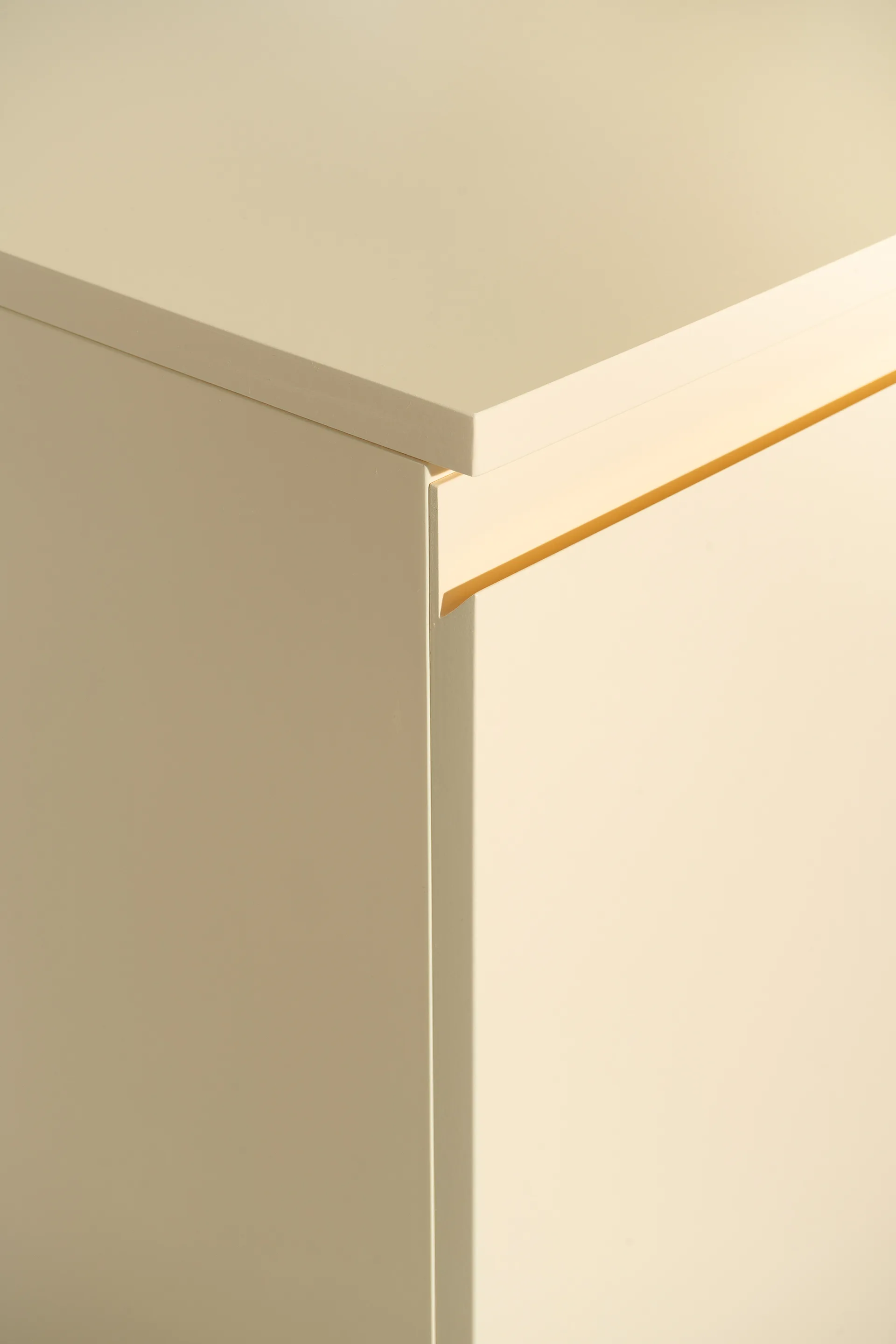A close-up shot of a cream-colored cabinet corner featuring a smooth matte finish and a sleek recessed finger-pull handle.